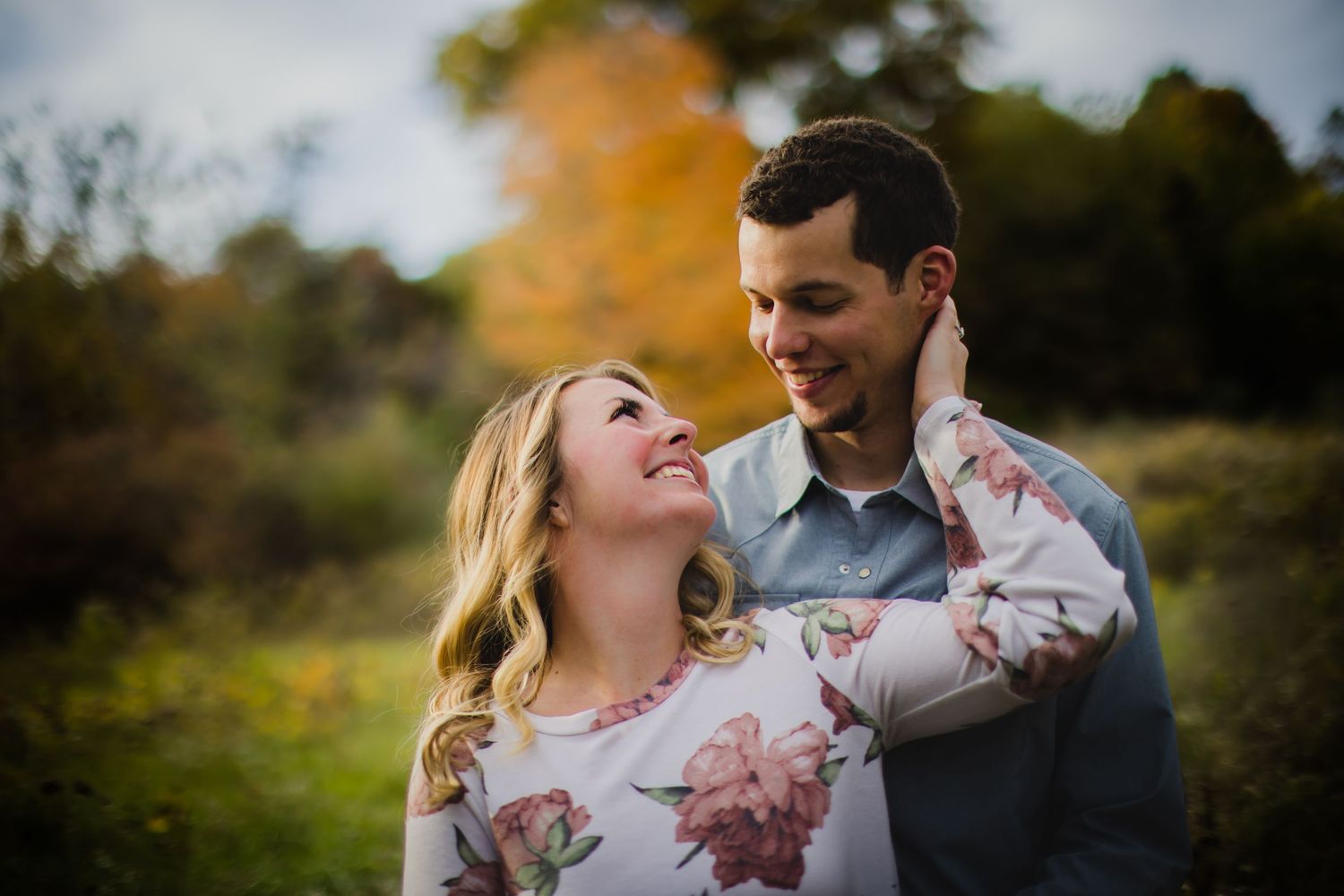 A candid engagement photo showing a couple sharing laughter against an autumn backdrop.