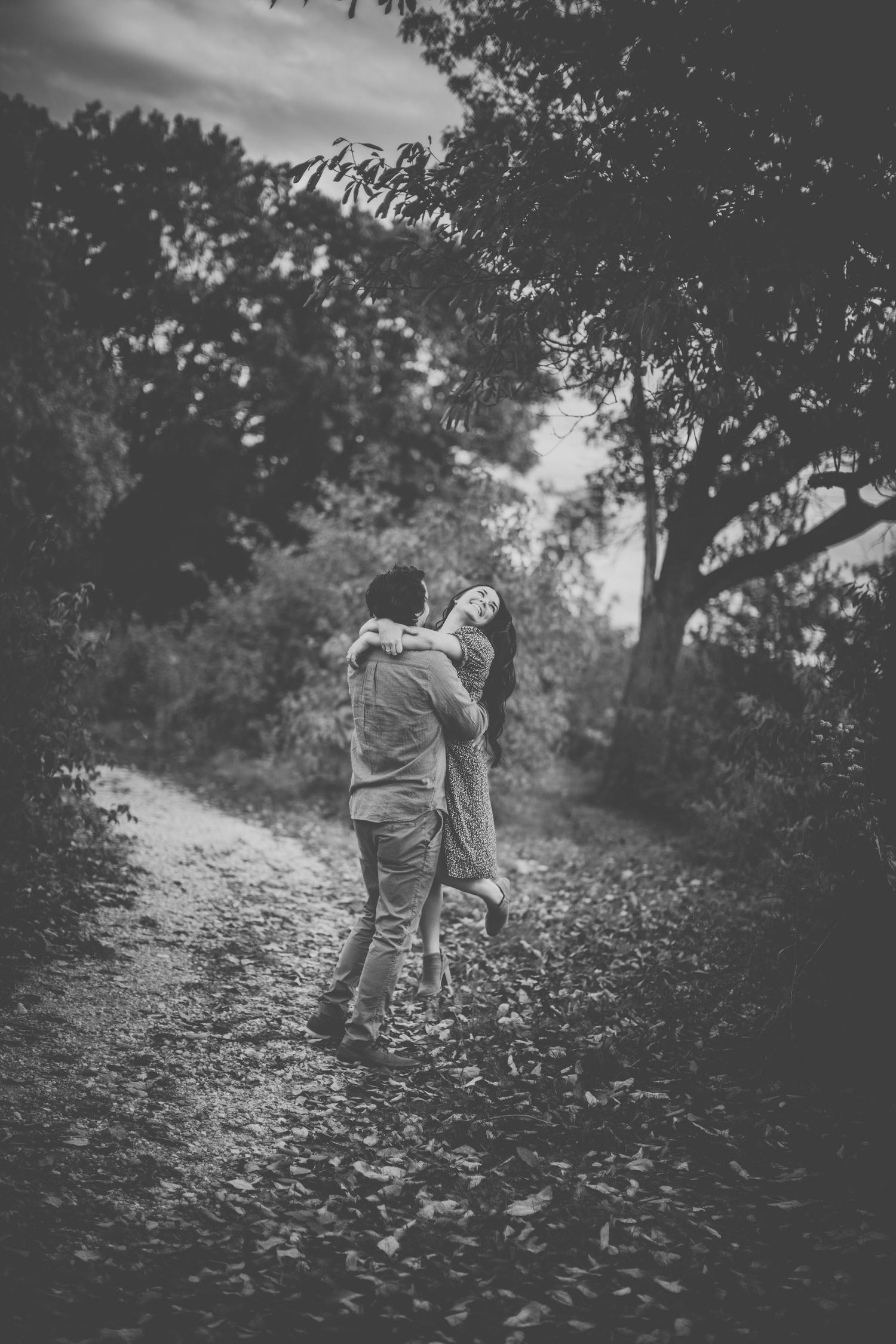 Black and white image of couple sharing joyful moment on forest trail.