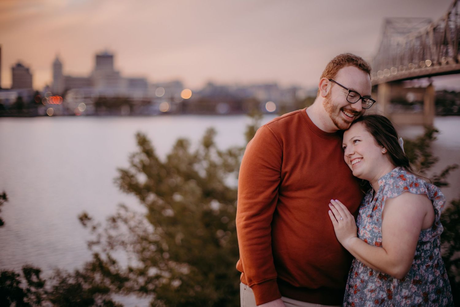 Romantic couple sharing an intimate moment at sunset by the waterfront with city skyline in background.