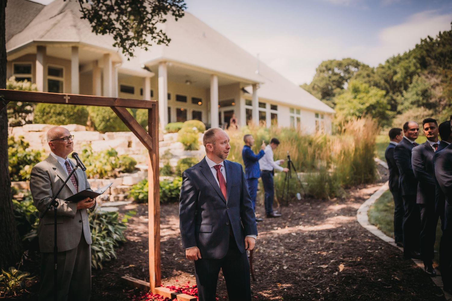 People gather outside a colonial-style building with white columns for a wedding ceremony.