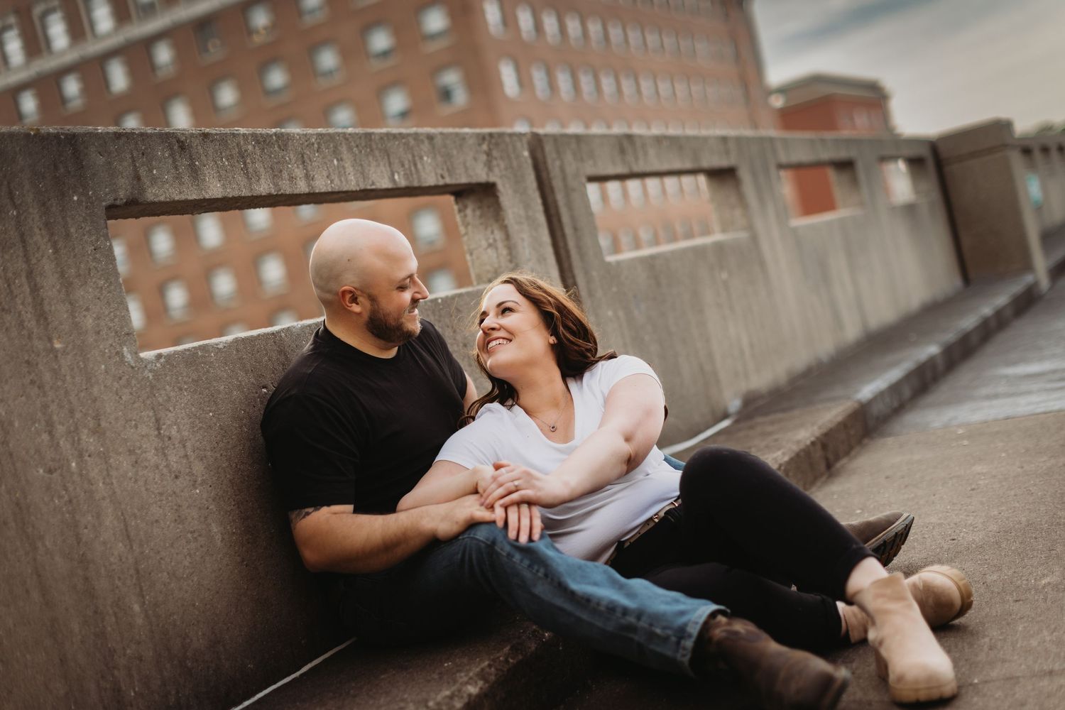 A couple shares a tender moment while sitting on a concrete ledge in an urban environment.