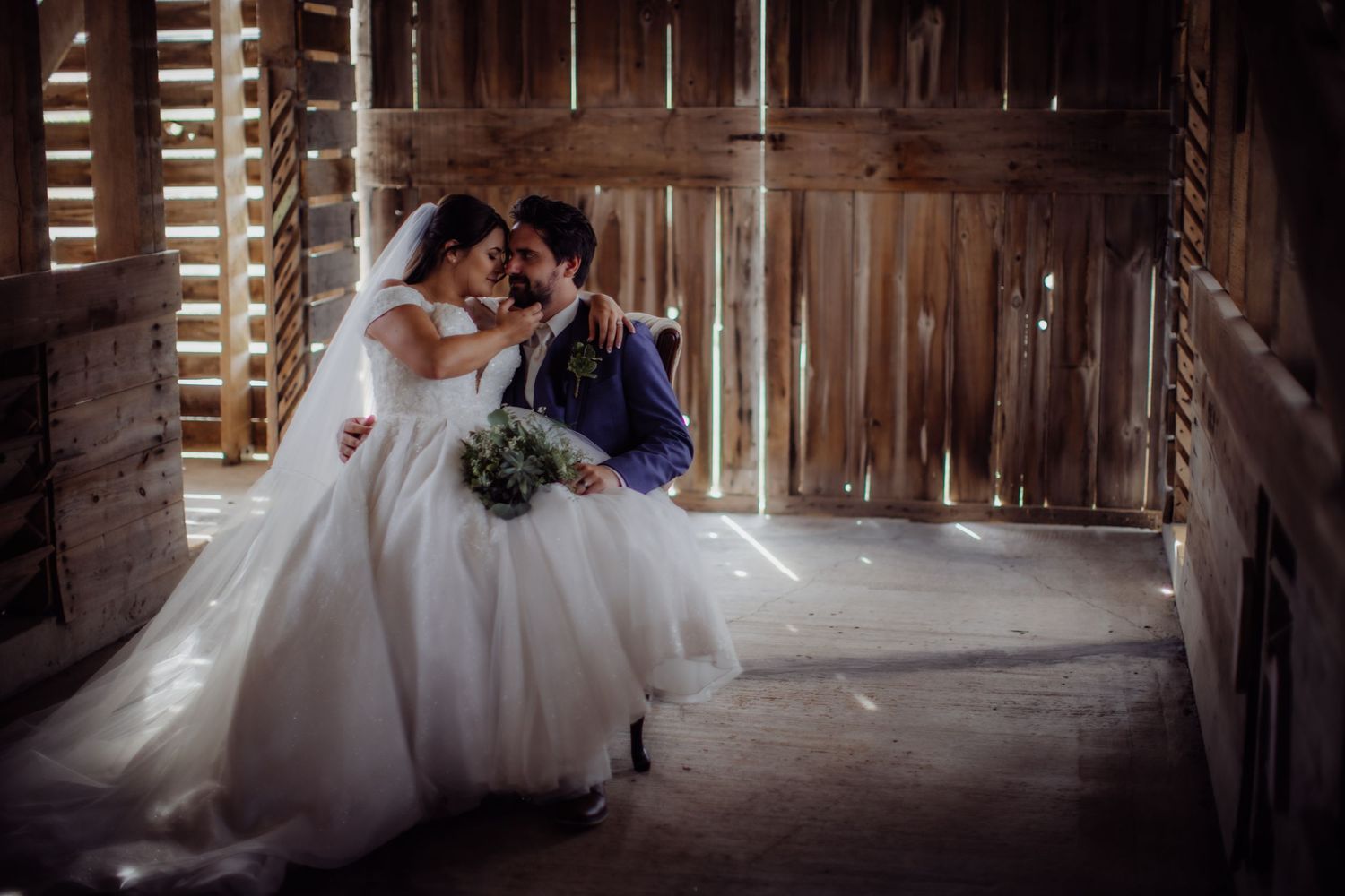 Newlyweds sharing a tender moment in a rustic wooden barn setting.