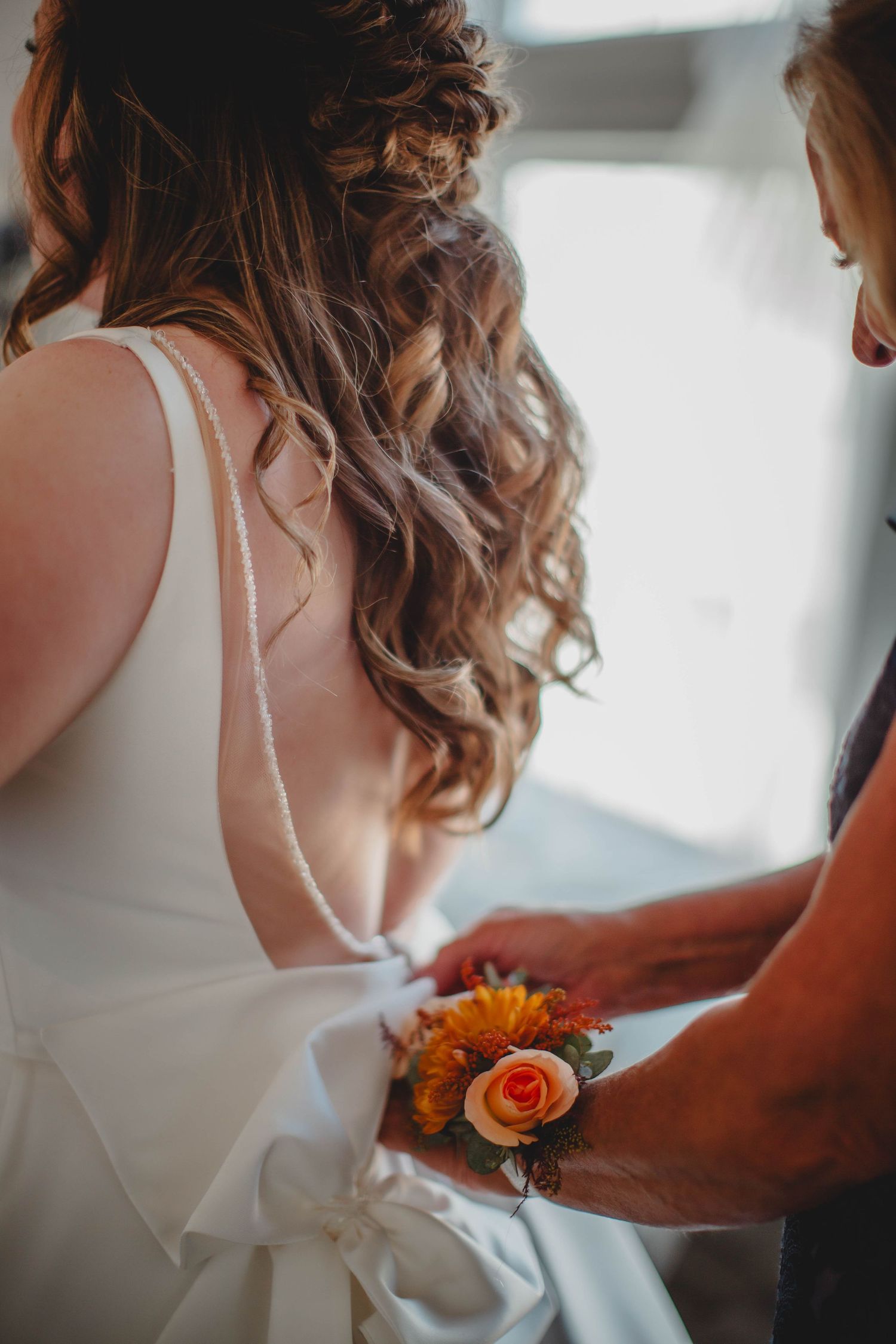 Back detail of a white wedding dress being adjusted, with orange and peach floral accents visible.