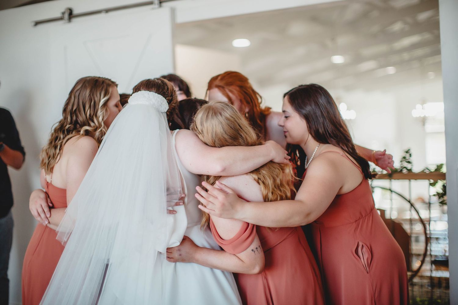 Bridesmaids in coral dresses and bride in white gather together for an emotional moment before the ceremony.