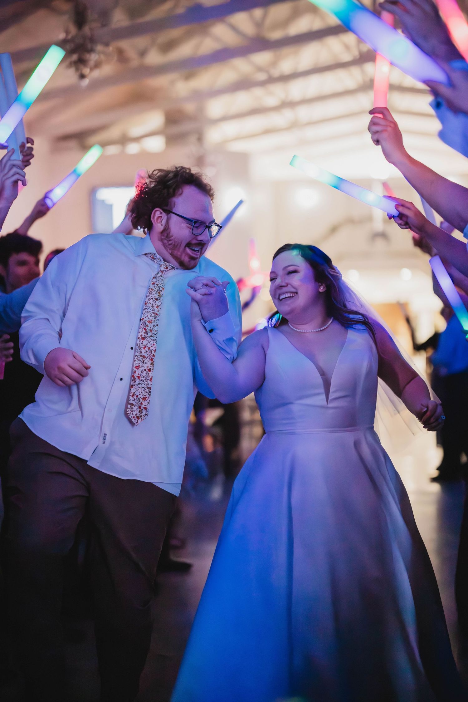 Wedding couple dancing energetically under glowing neon lights at their reception celebration.