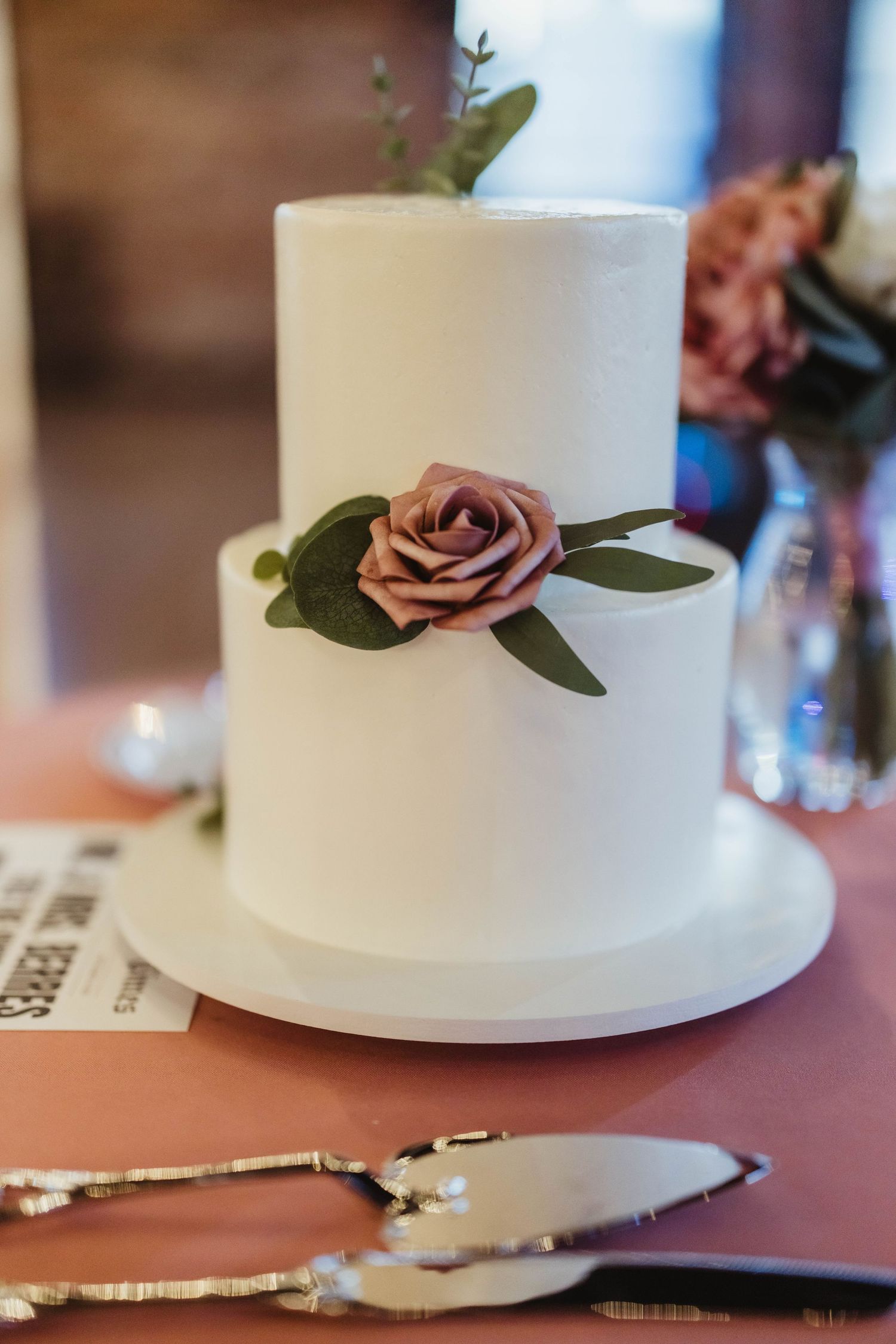 Simple white wedding cake decorated with a single dusty rose flower and green leaves.