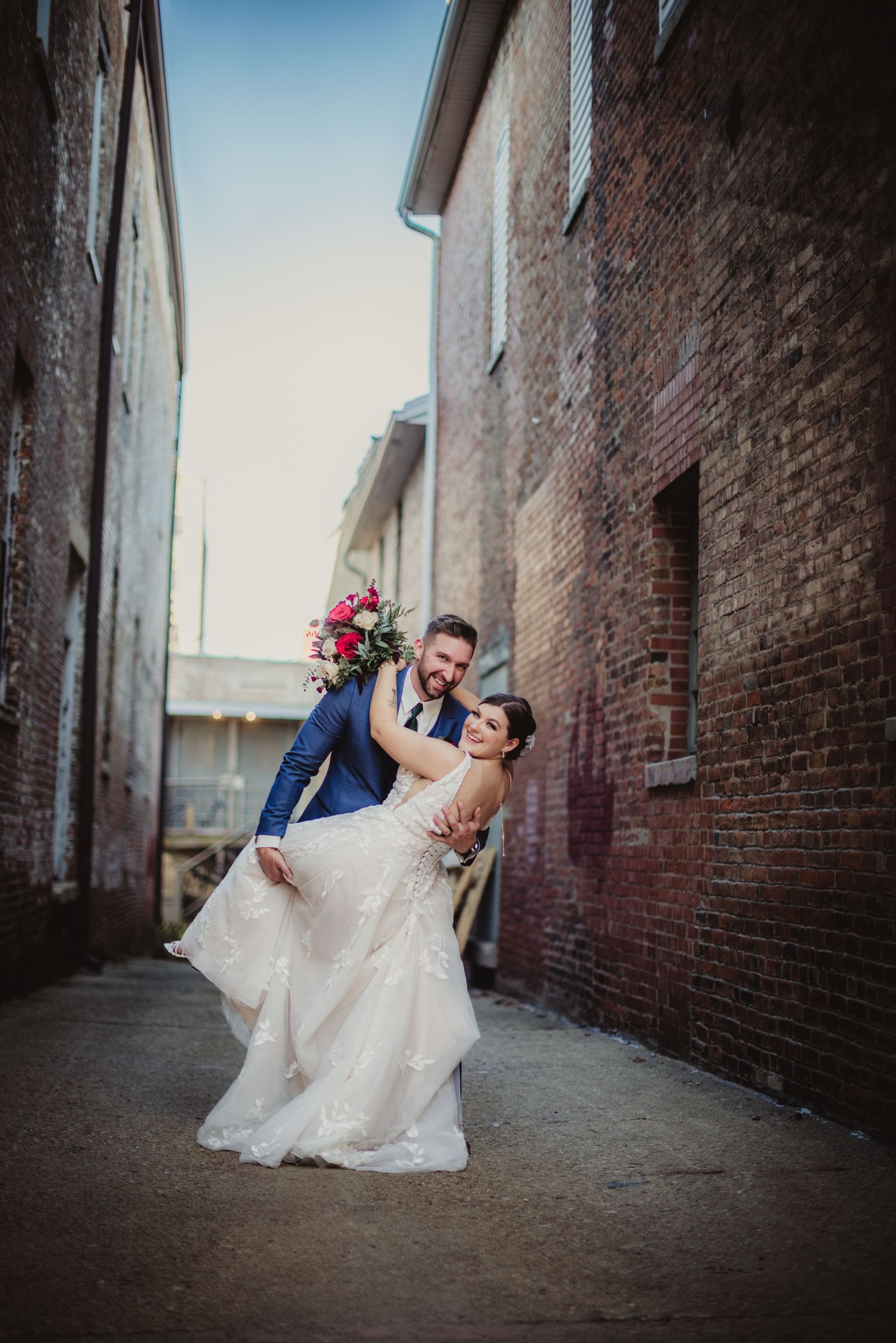 Dramatic wedding portrait against industrial brick walls with romantic dip pose.