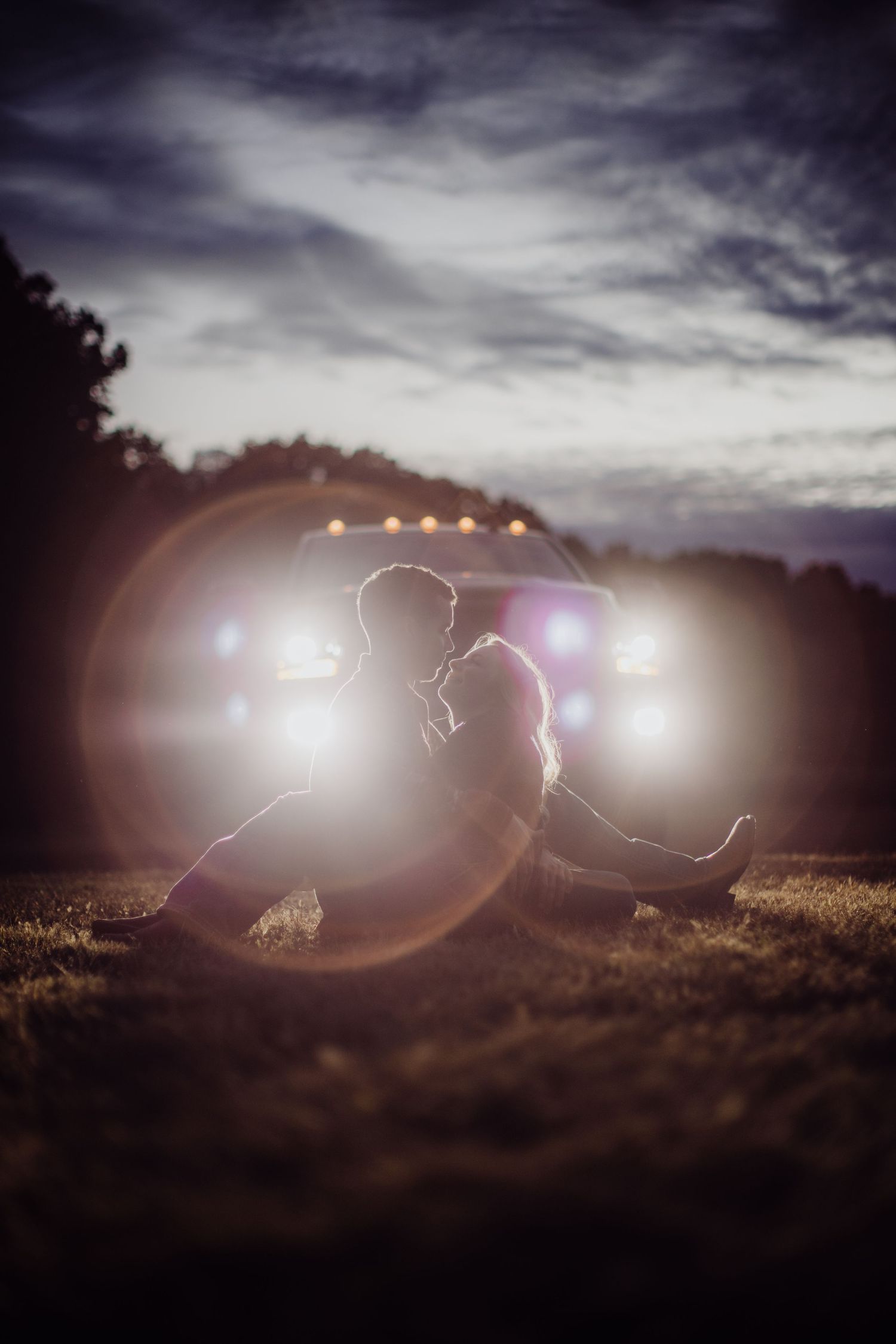A romantic silhouette against dramatic clouds with car headlights creating atmospheric lighting.