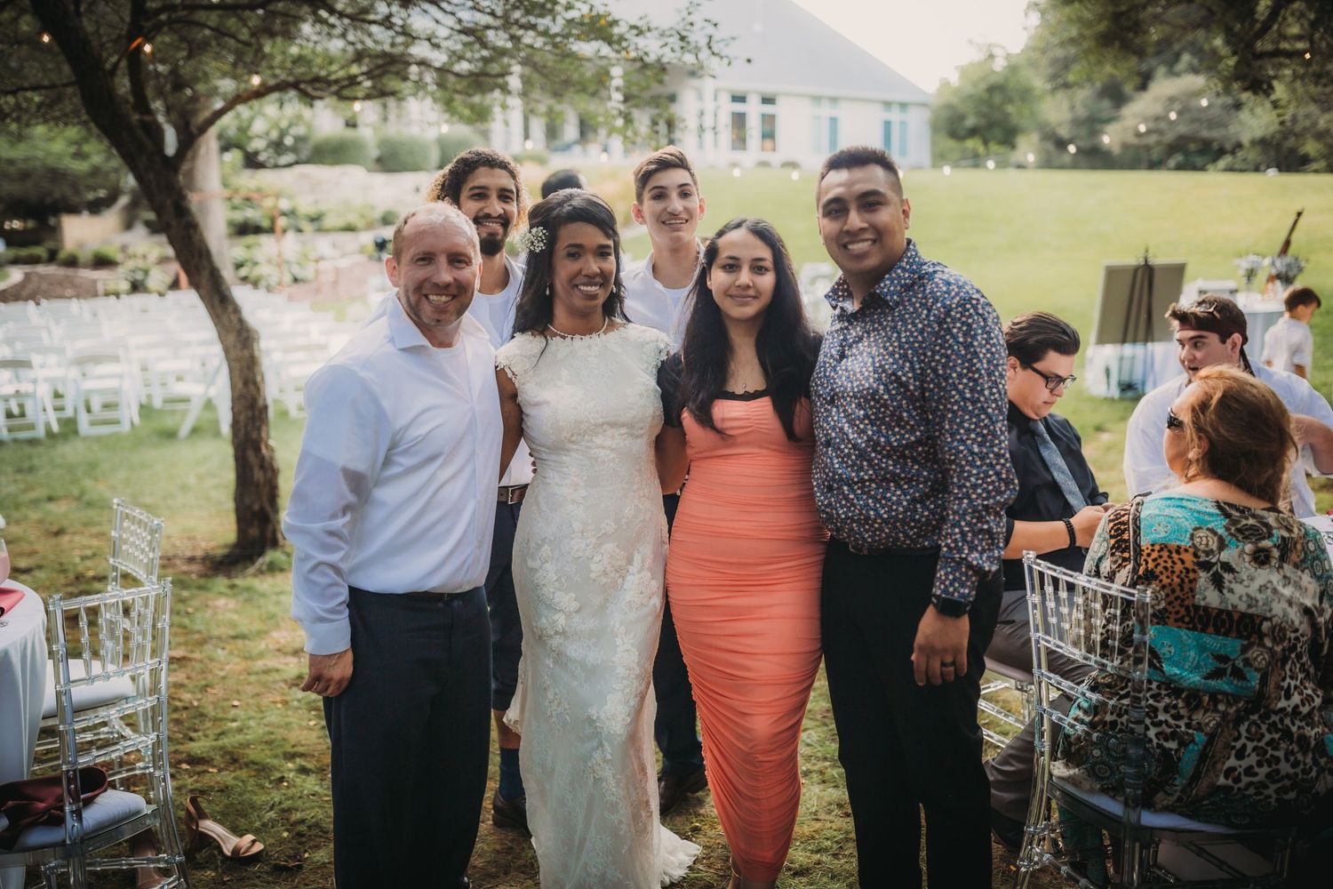 Wedding guests gathered for a group photo on a lawn with white chairs in the background.