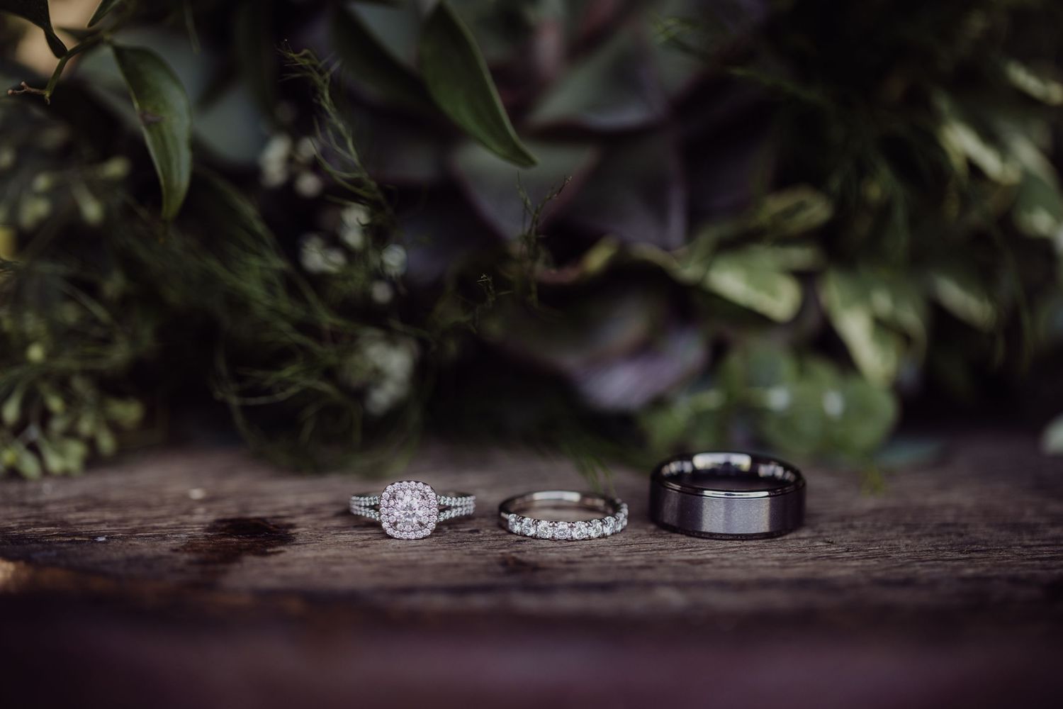 Three wedding rings arranged with greenery on dark wooden surface.