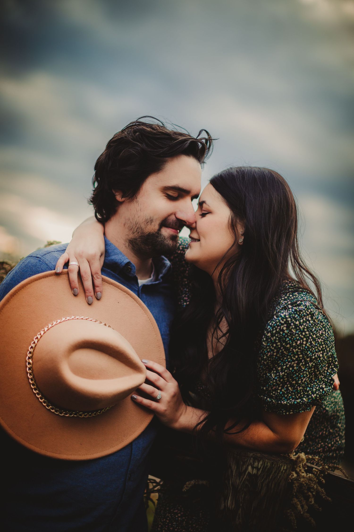 Intimate moment shared between couple with brown hat against cloudy sky.