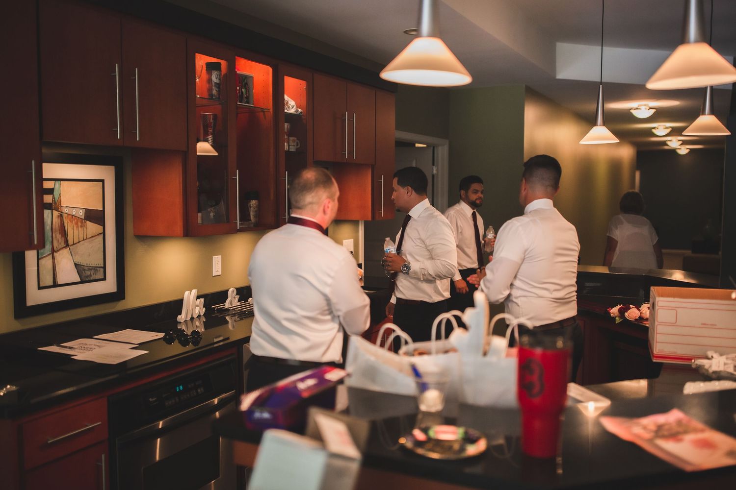 Several people gathering in modern kitchen with dark wood cabinets and pendant lighting.