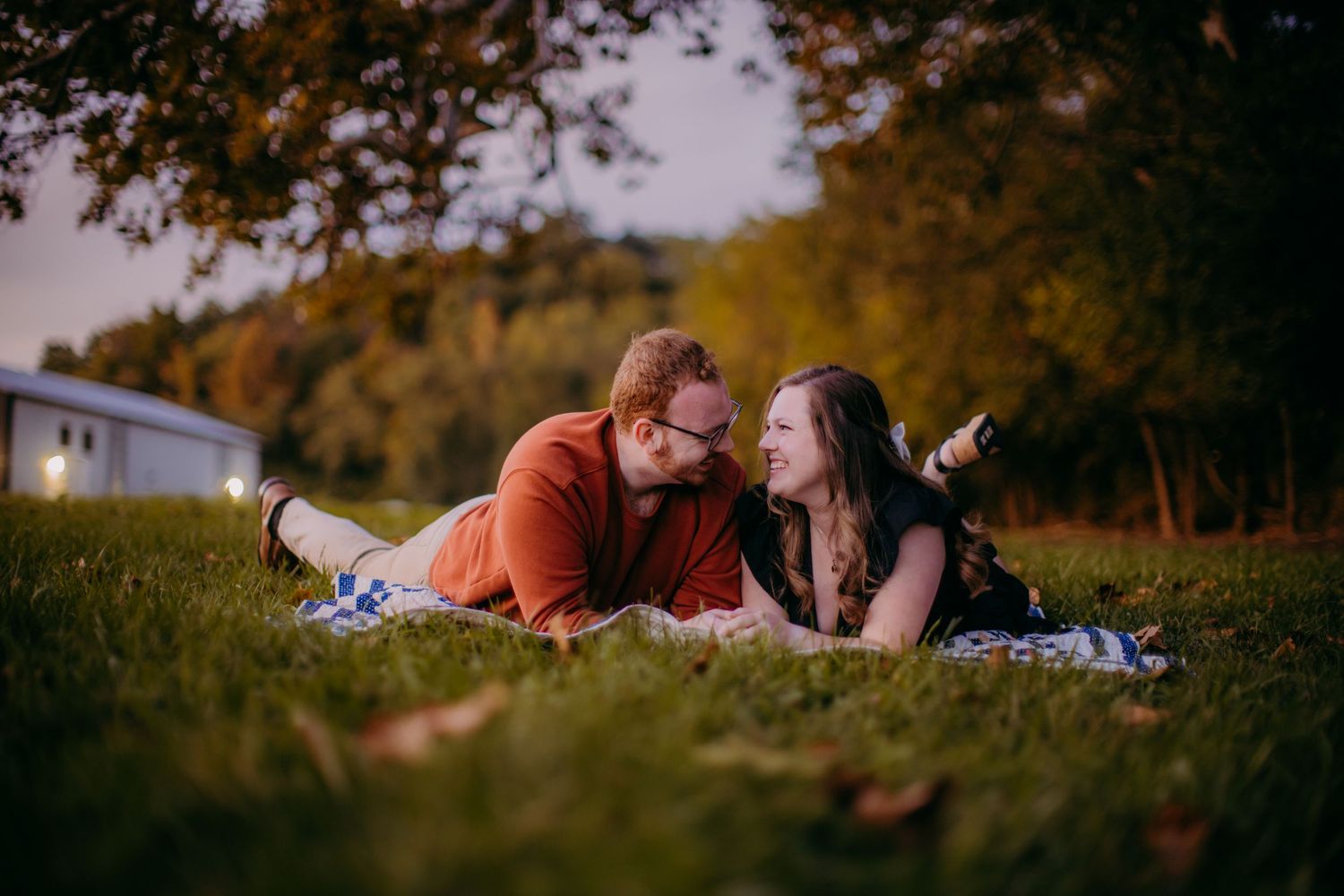 Couple lying together on blanket in autumn grass during sunset photoshoot.