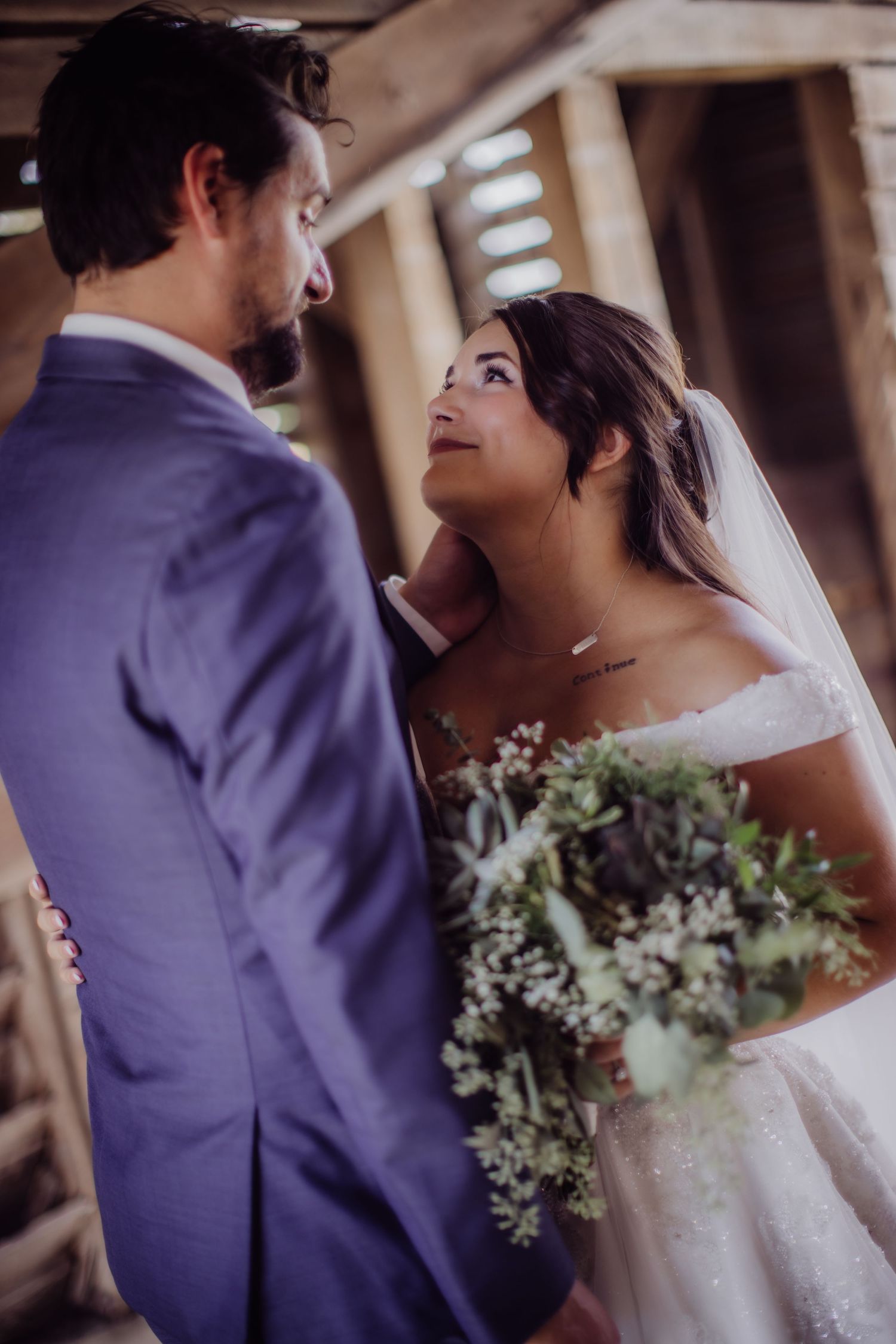 Intimate moment between newlyweds captured in rustic barn with wooden details.