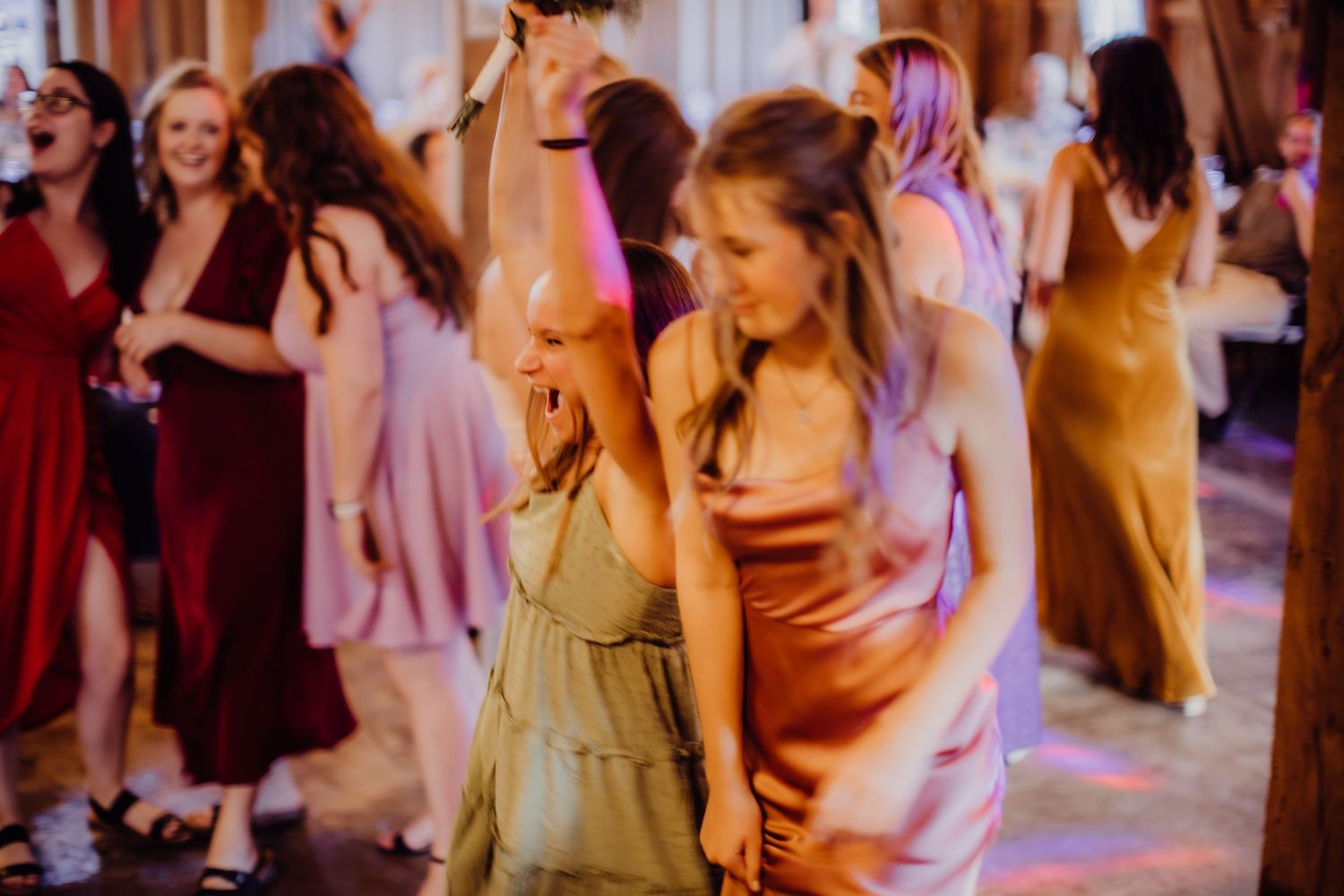 Wedding guests dancing together at a rustic barn reception with festive lighting.