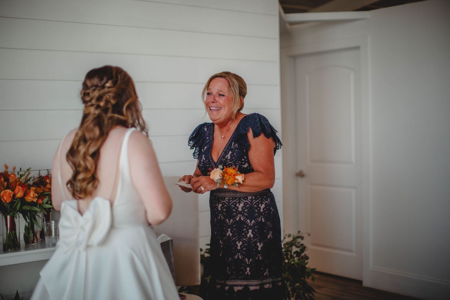 Two people interact during a wedding preparation moment with orange floral arrangements in background.