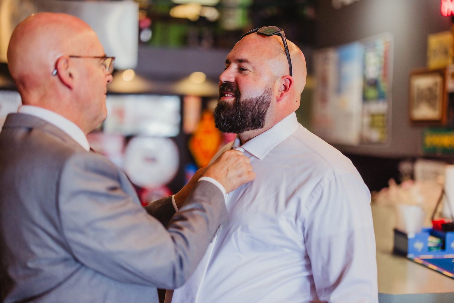 Two people sharing a laugh while fixing each other's formal attire.