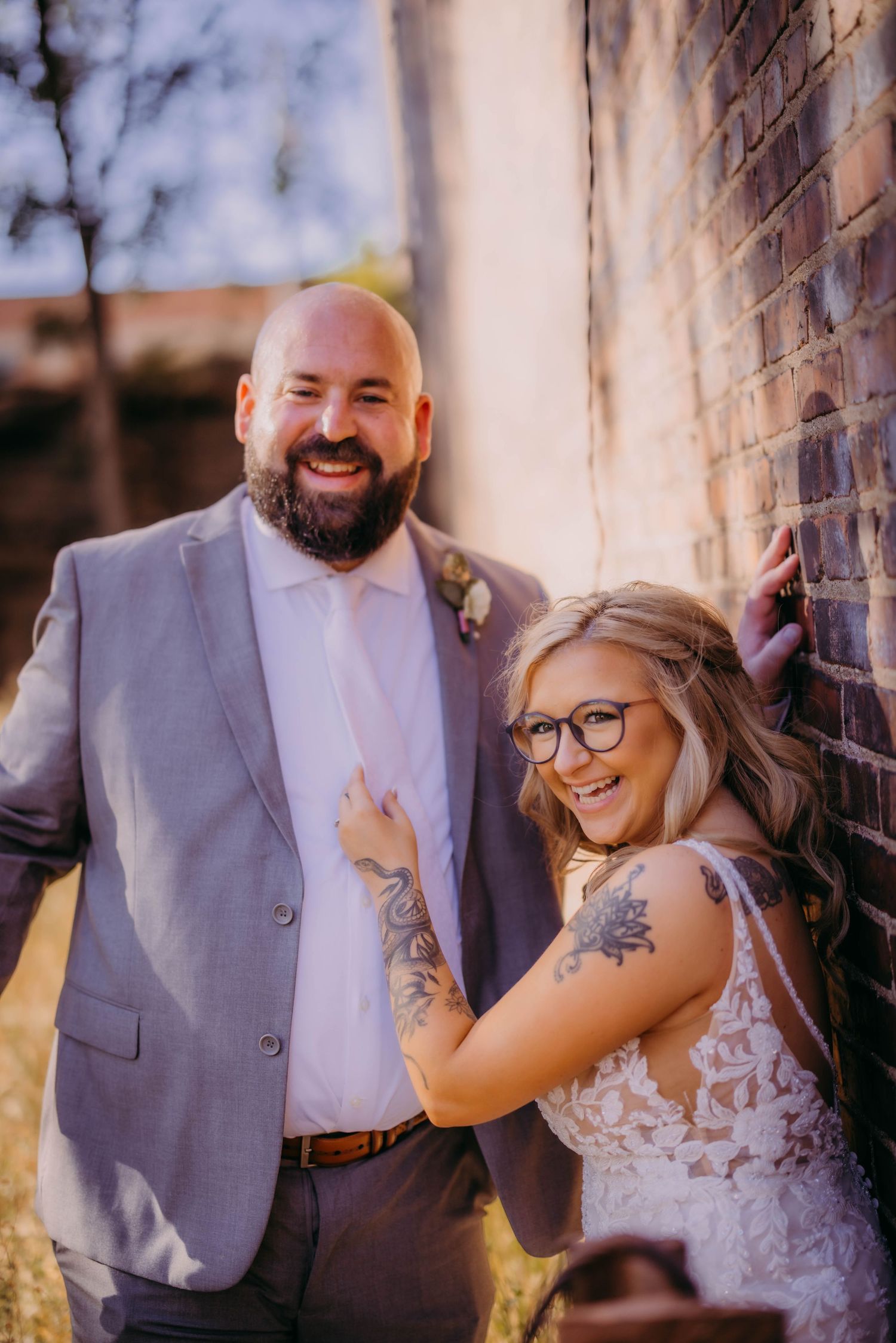 A joyful wedding portrait against a brick wall showing the couple's genuine happiness.