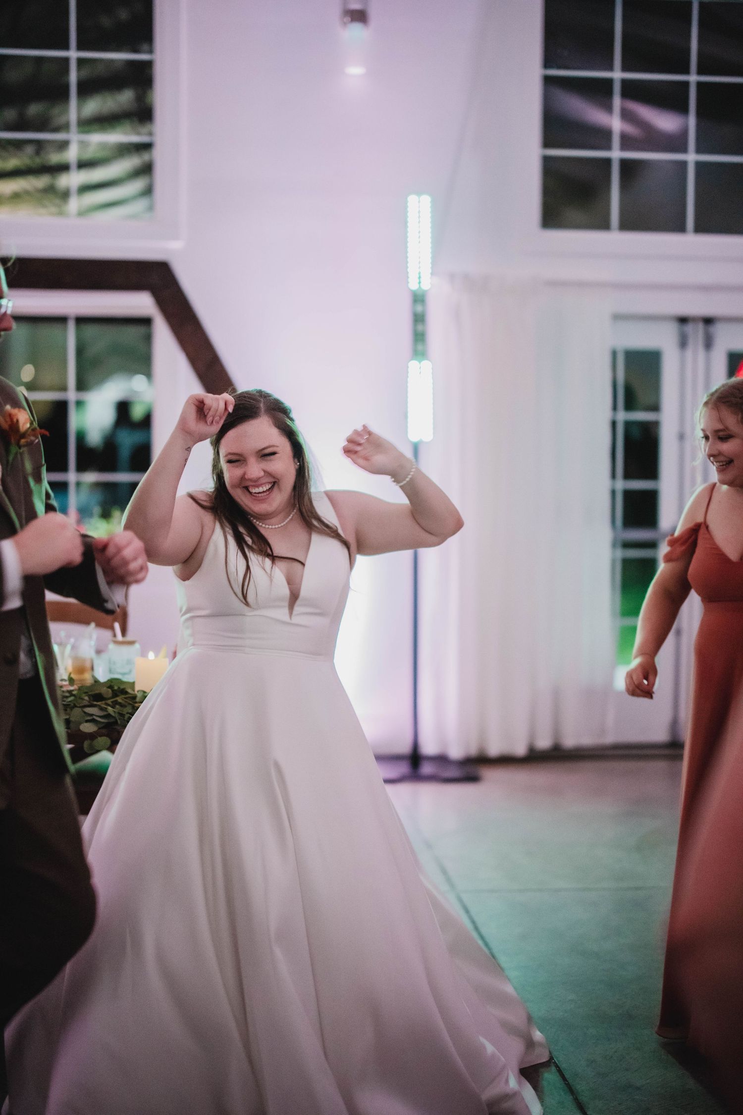 A bride in a sleeveless white gown dances joyfully at her wedding celebration.
