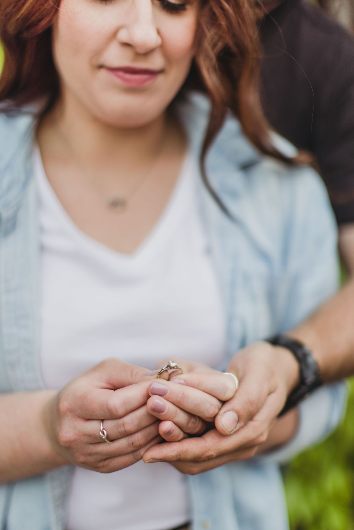 Close-up shot of hands holding a ring with a light blue chambray shirt and greenery in background.