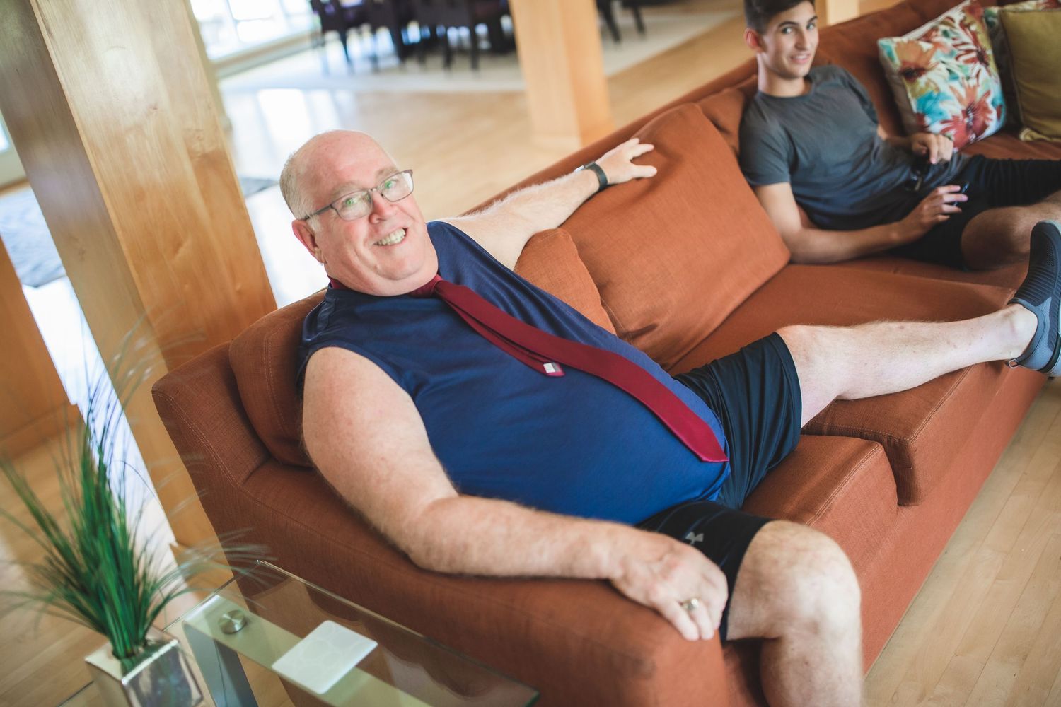 Person relaxing on brown couch wearing casual summer attire with red tie.