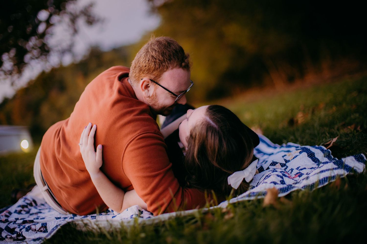 Romantic evening photoshoot of couple sharing tender moment on patterned blanket.