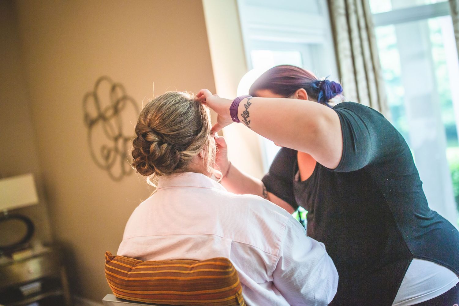 Hair stylist working on bridal preparation in sunlit room.