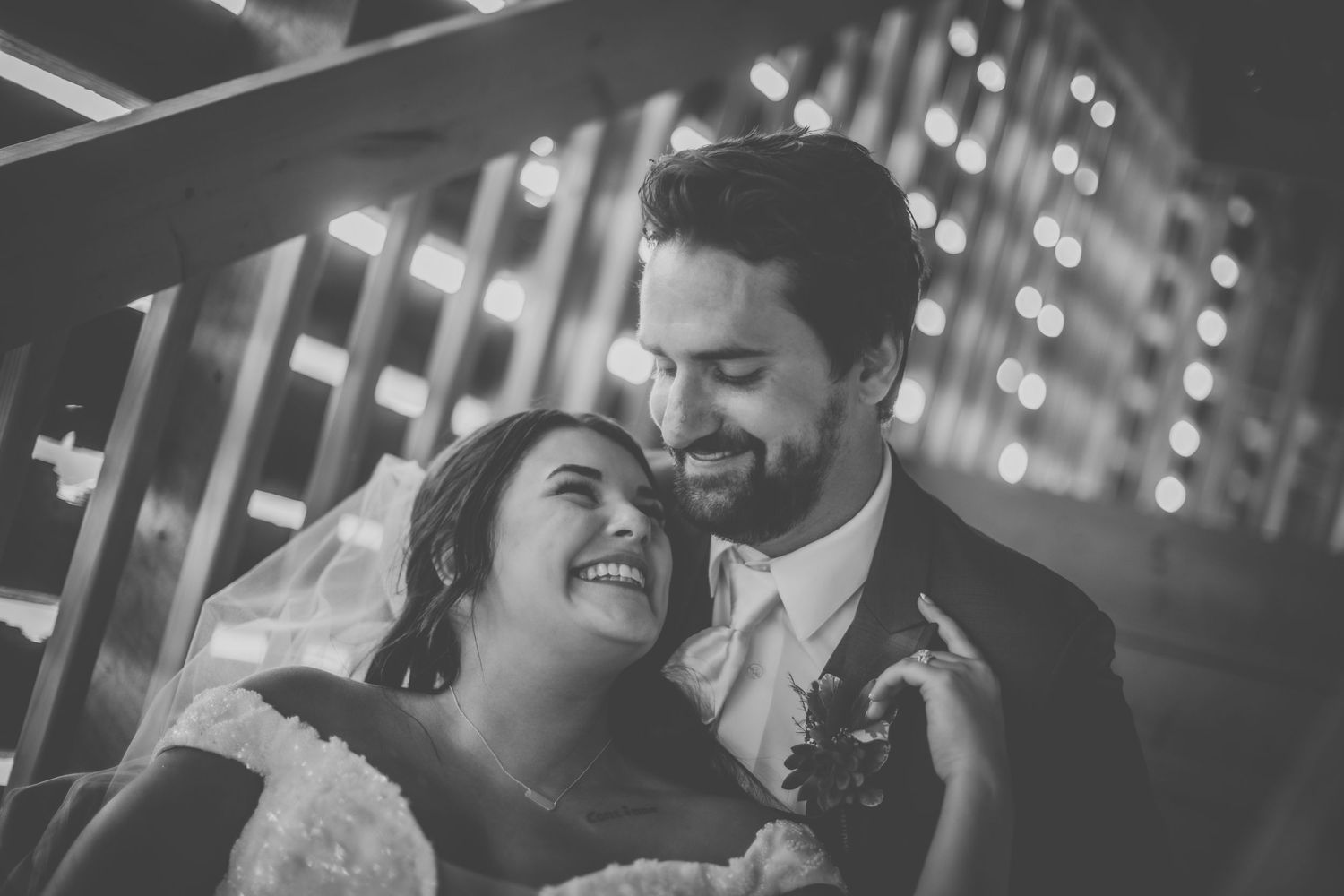 Black and white wedding portrait with string lights creating magical atmosphere in rustic setting.