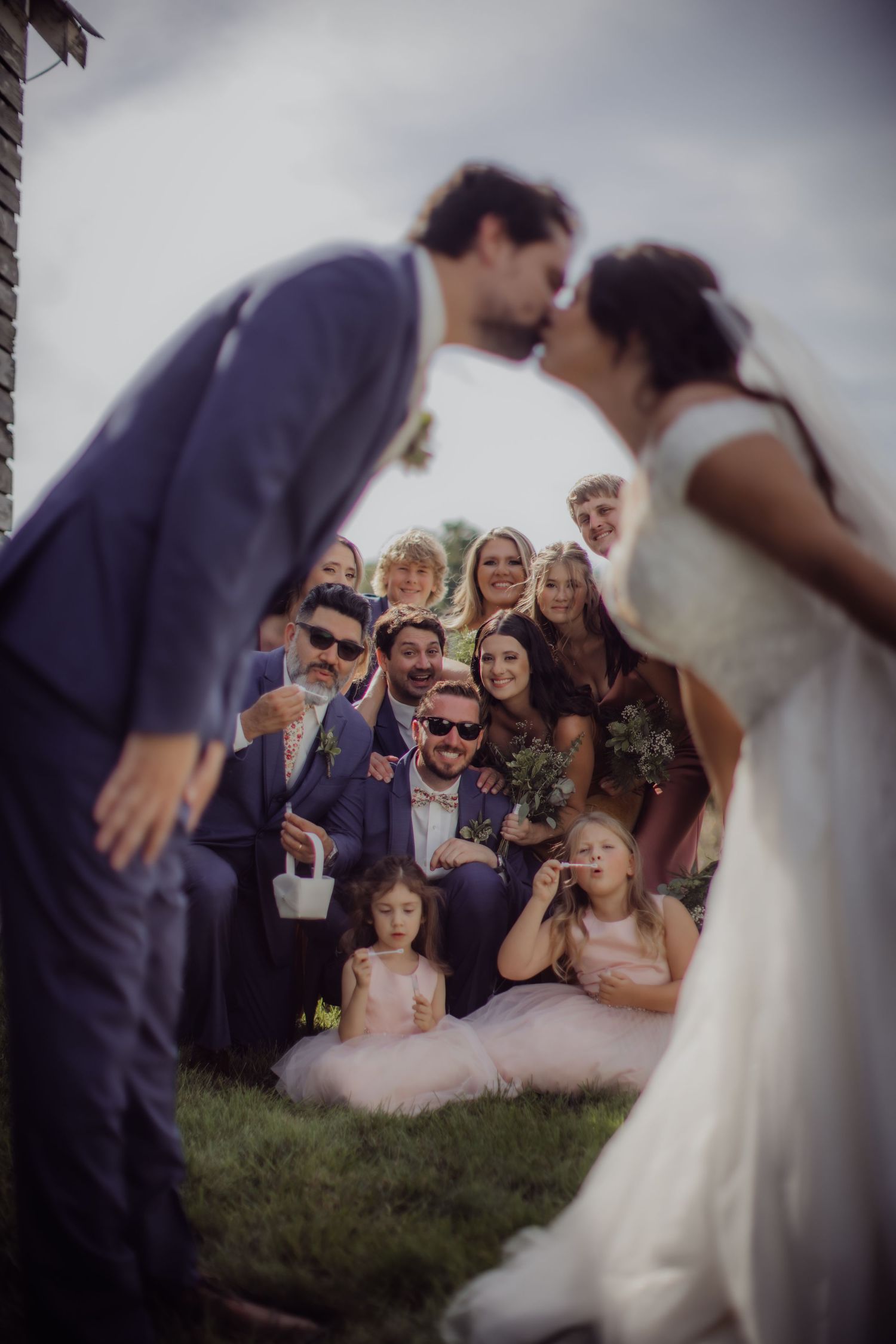Creative wedding photo composition through veil with guests gathered on grass.