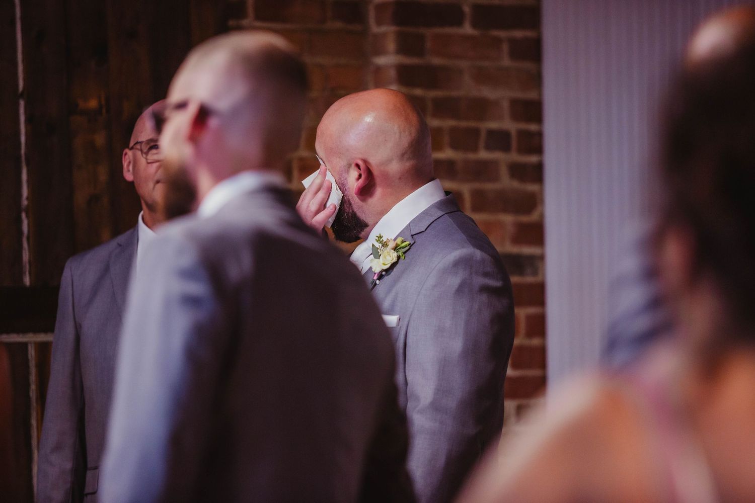 Wedding party members in grey suits share an emotional moment during the ceremony.