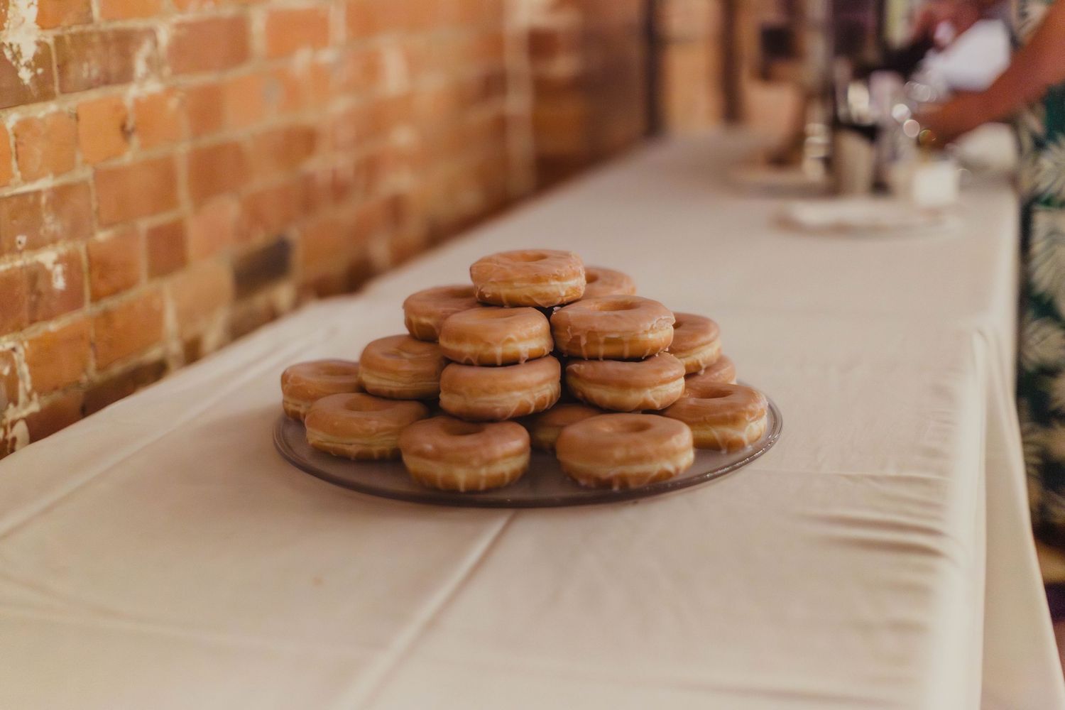 Stack of brown macarons displayed on white tablecloth against brick wall.