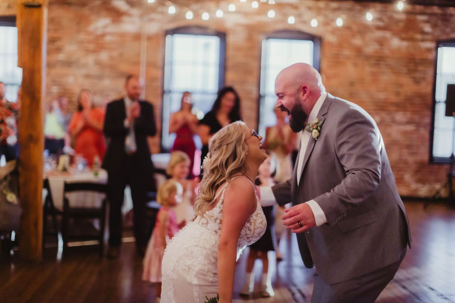 Wedding couple dancing in rustic venue decorated with string lights.