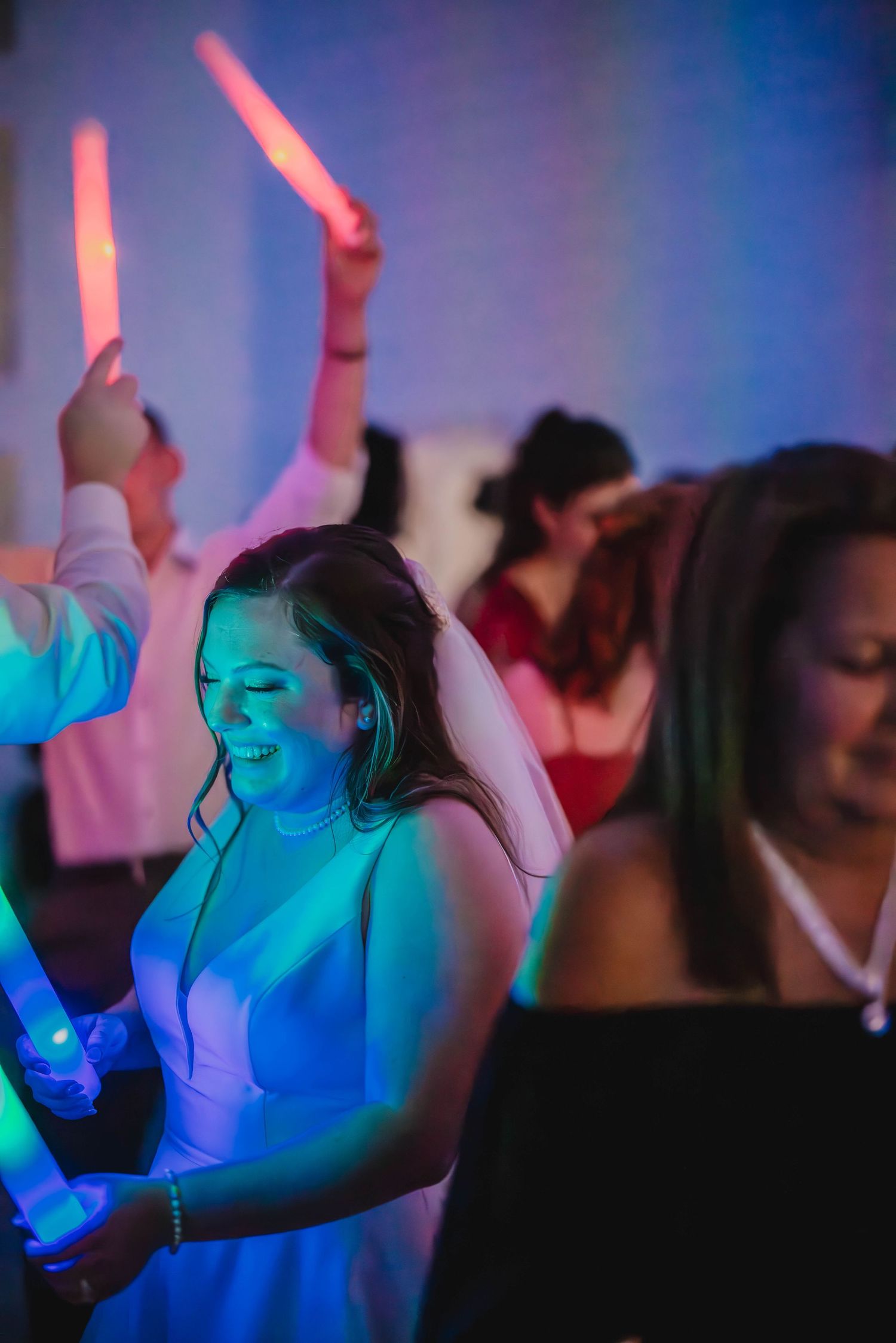 Dancers holding glowing LED sticks while celebrating under vibrant blue and pink lights.