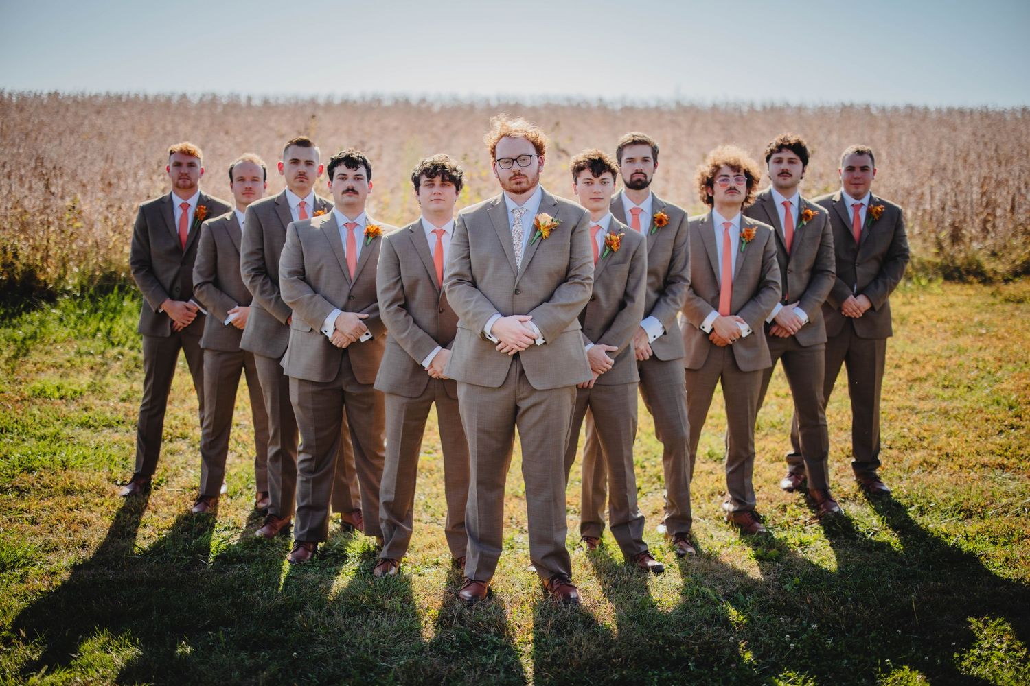 Wedding party groomsmen group photo in gray suits against rural backdrop.