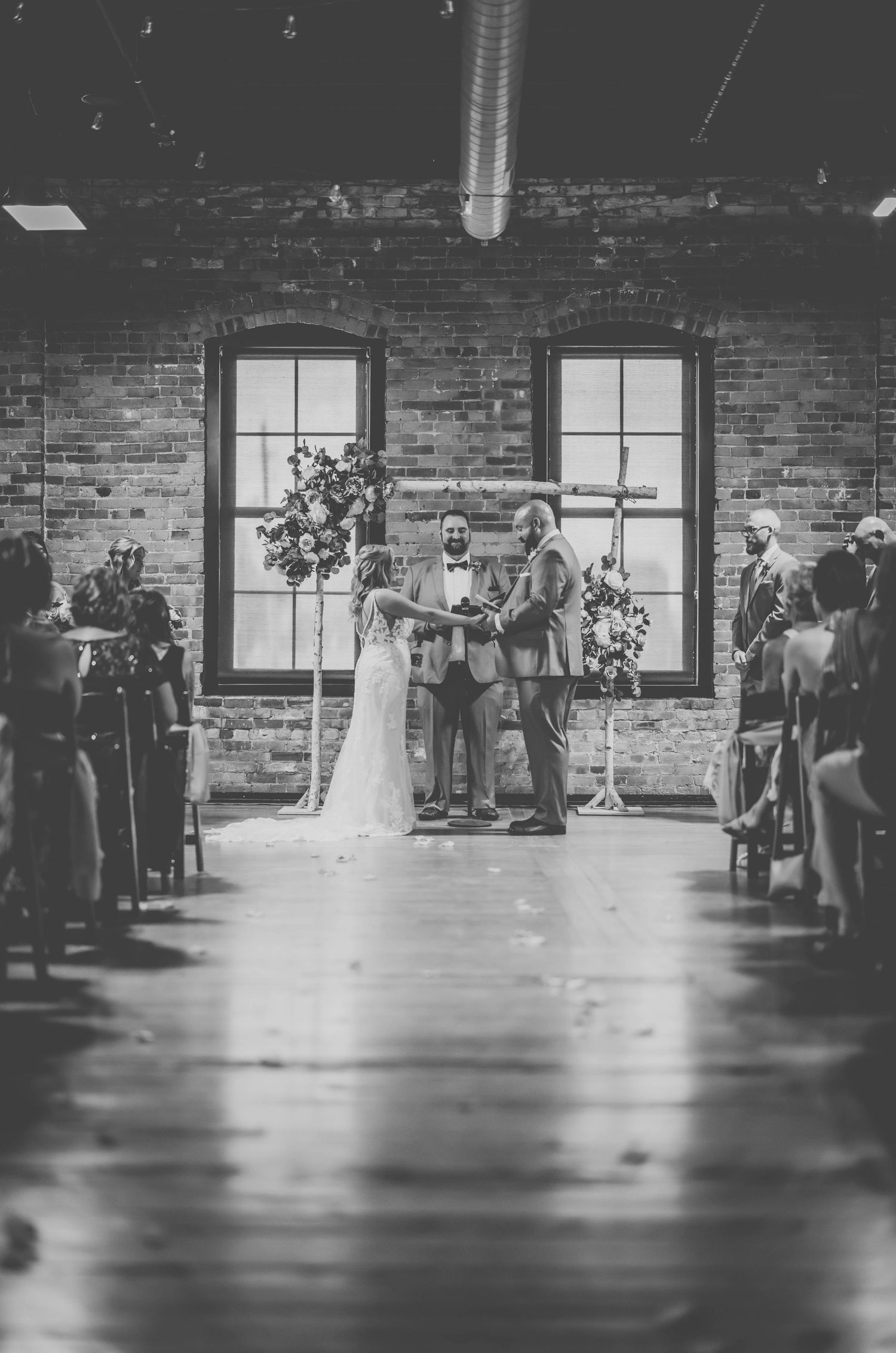 Black and white photo of wedding ceremony in rustic venue with natural lighting.