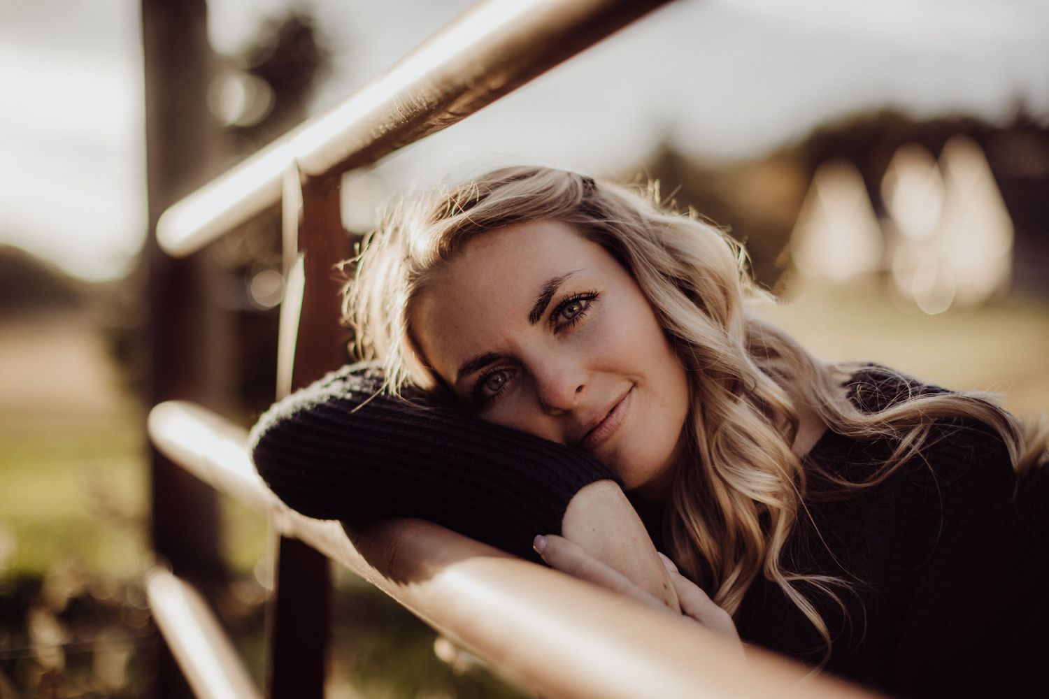 A close up portrait of a woman with wavy hair resting on wooden fence.