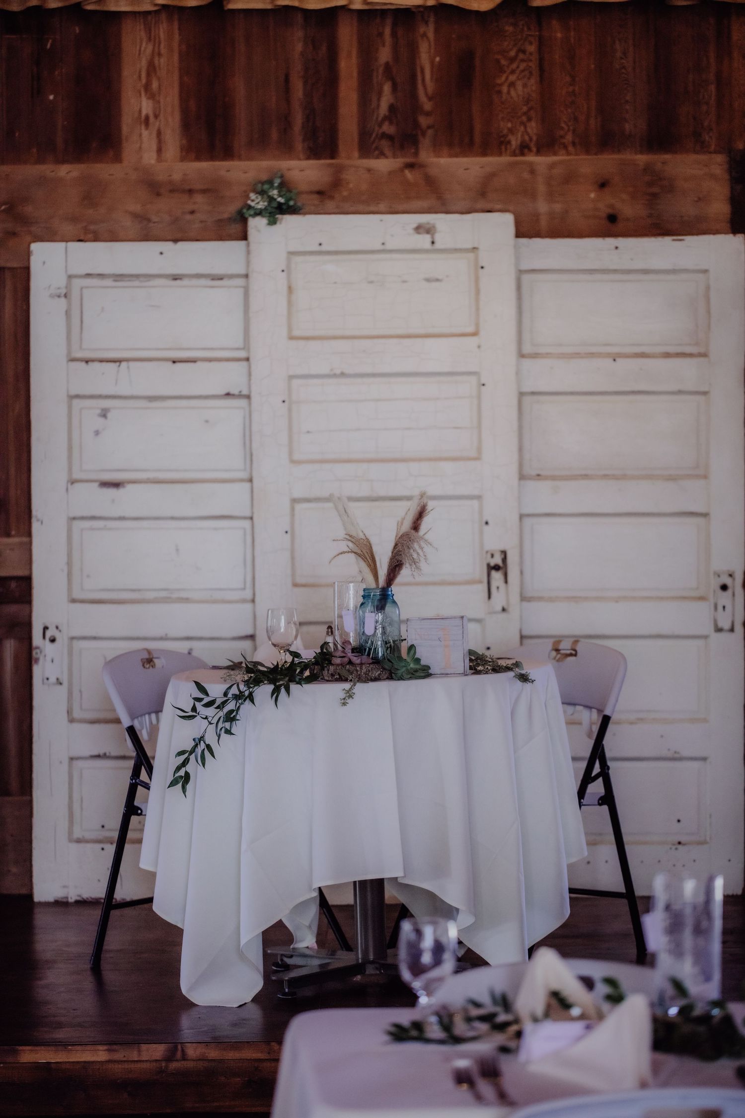 White reception tables set against rustic white paneled walls in a barn venue.