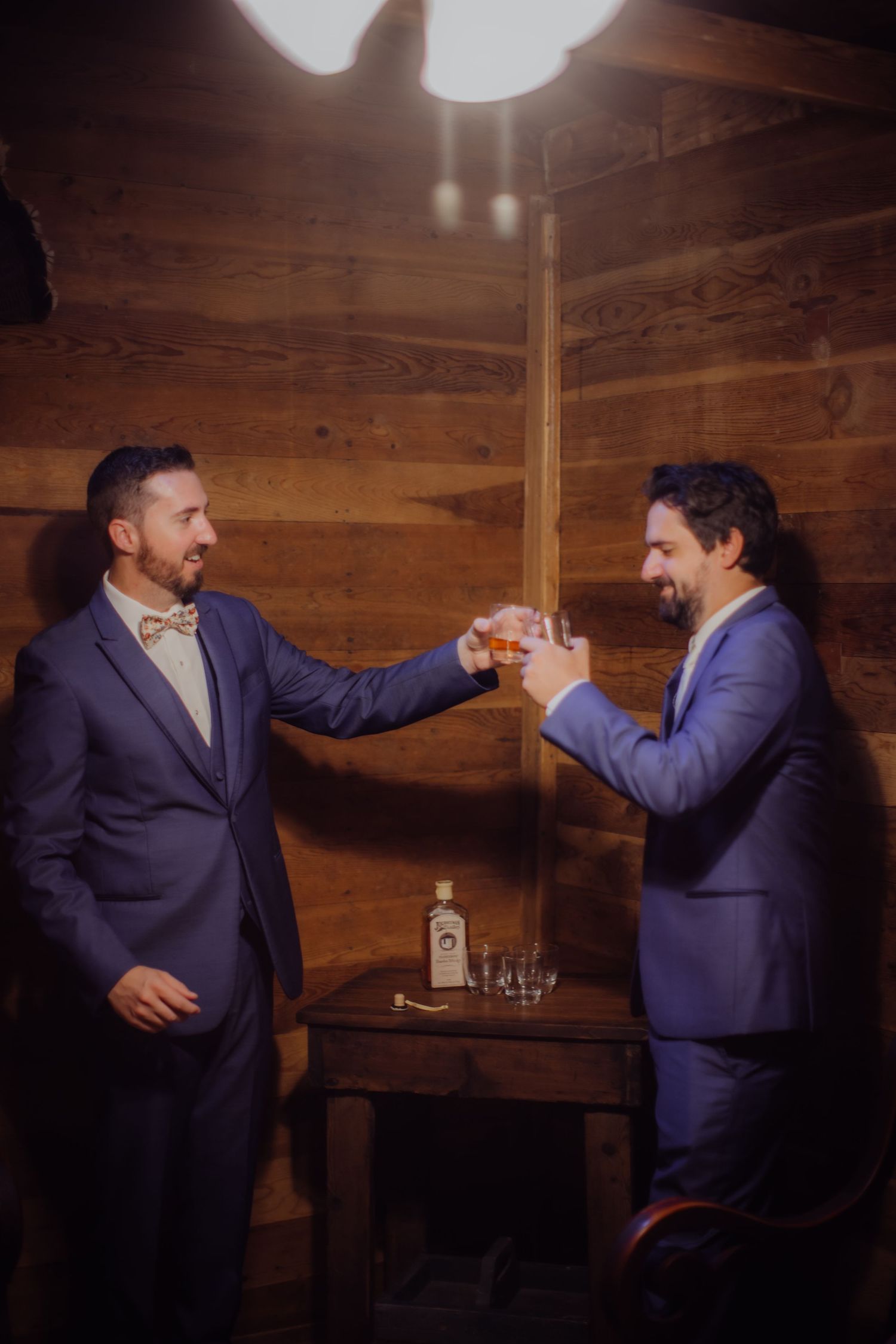 Wedding party members sharing a toast in navy suits against wooden wall.