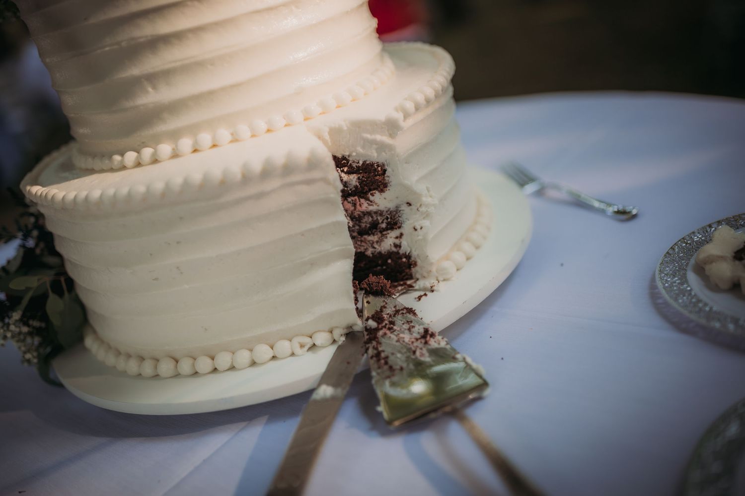 Close-up of a sliced white wedding cake with decorative piping showing layers inside.