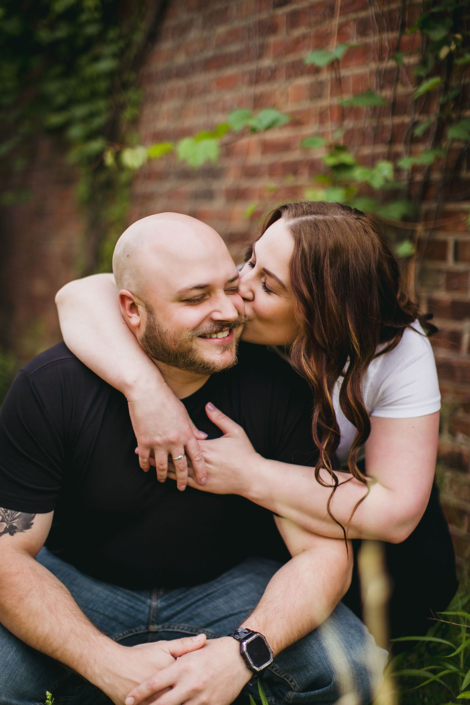 Sweet candid moments between couple during outdoor photoshoot by brick wall.