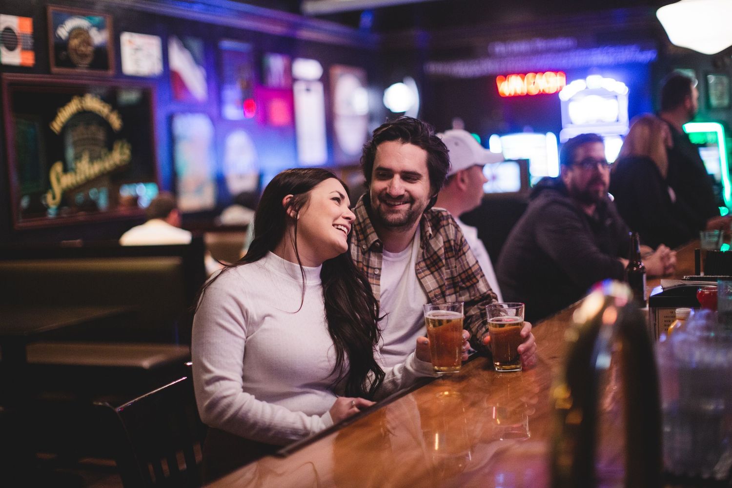 People enjoying drinks at a dimly lit bar with neon signs and ambient lighting.