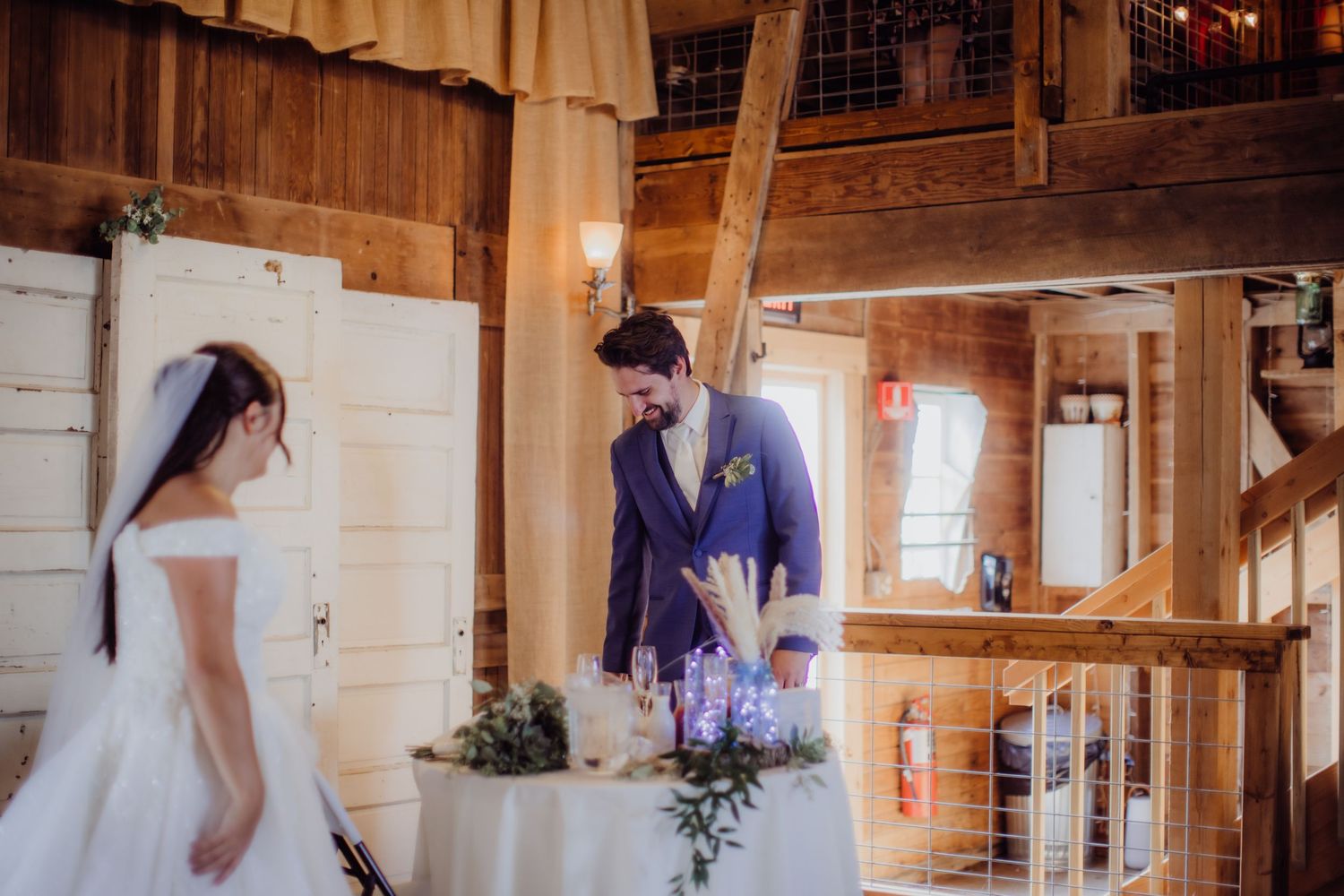 Wedding couple stands together in rustic barn setting with warm lighting and wooden walls.