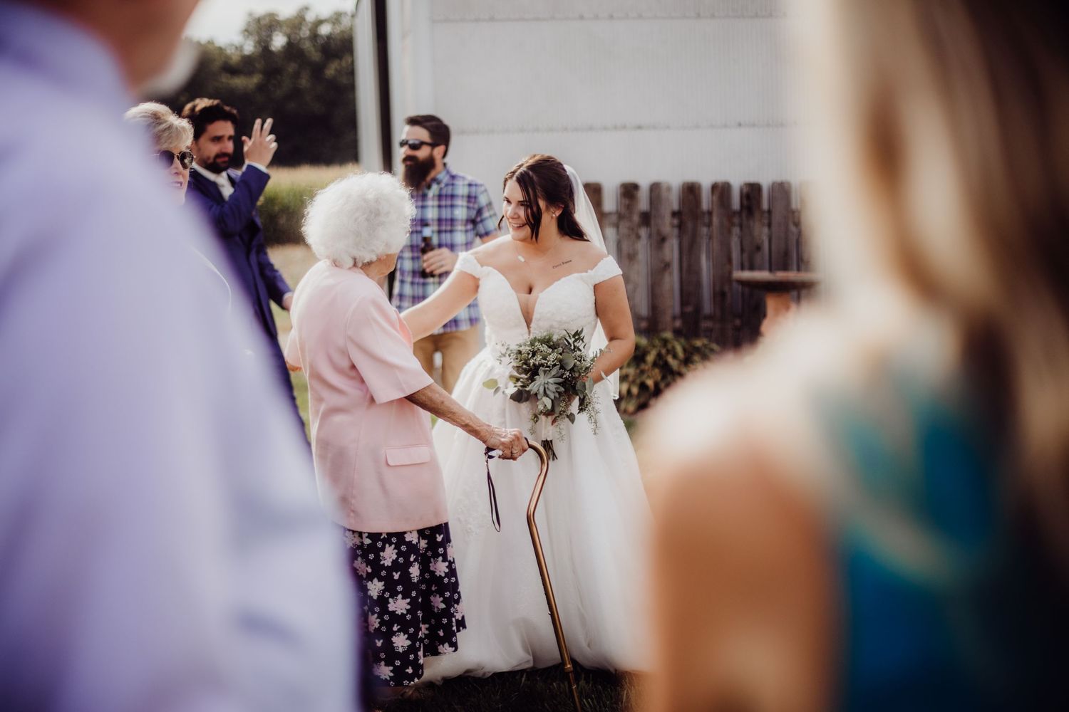 Wedding party members mingle during an outdoor reception near a white building.