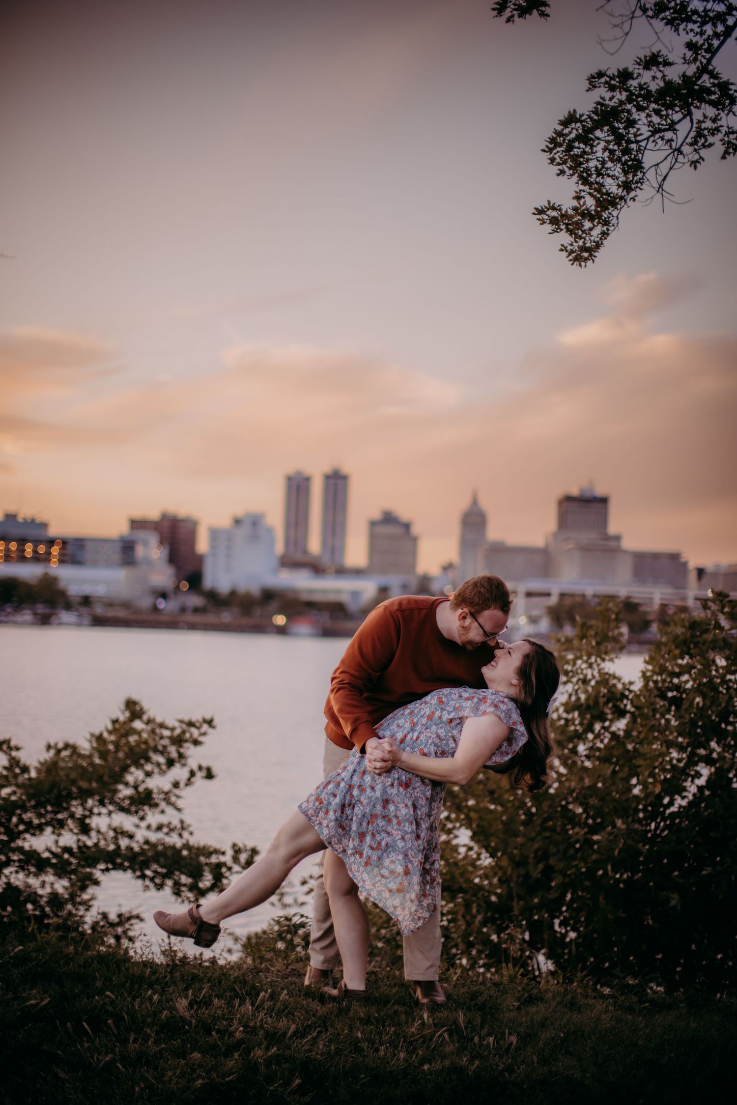 Couple sharing an intimate dip pose against an urban waterfront backdrop during golden hour.