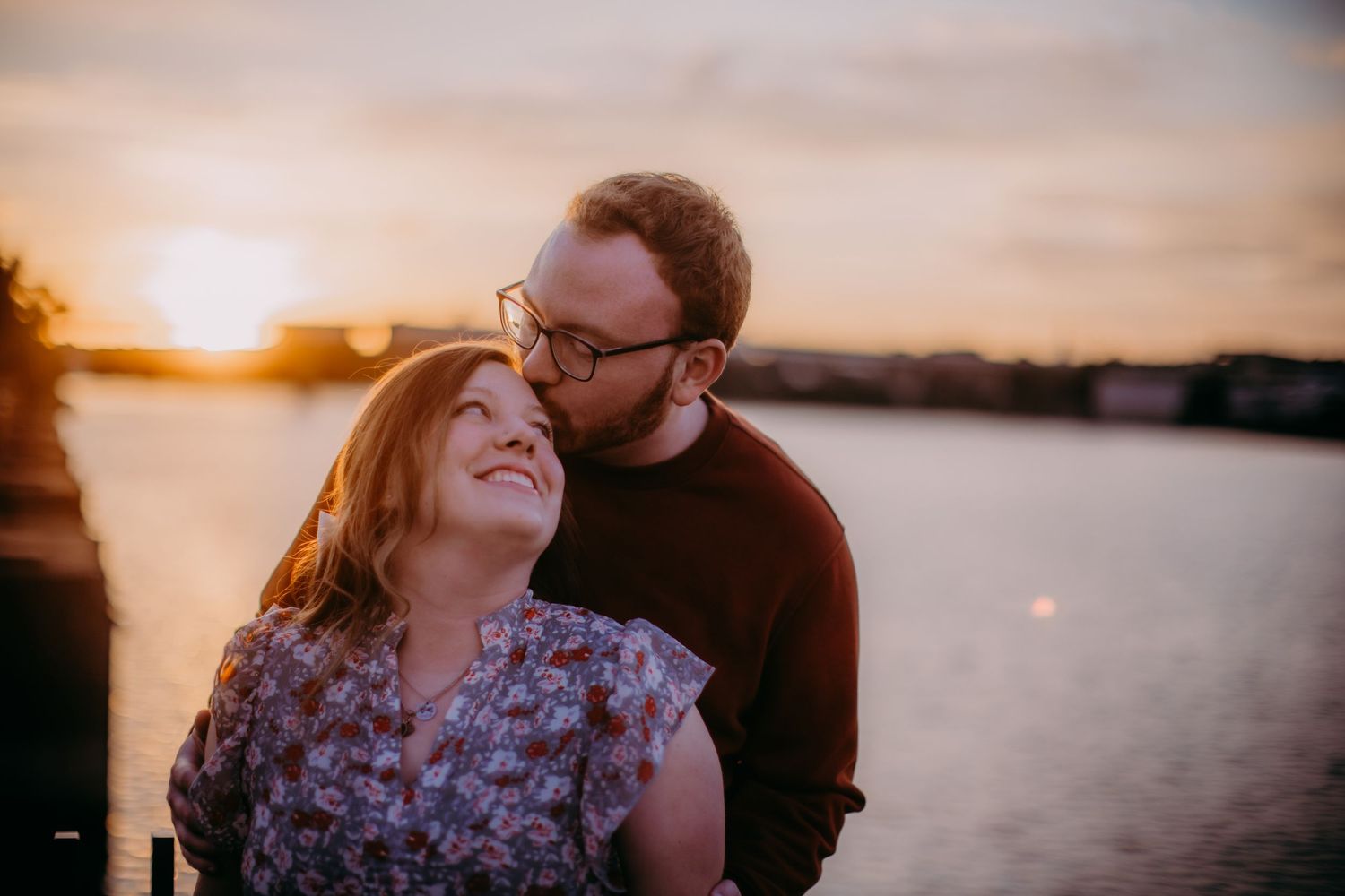 Romantic couple embraces during golden sunset by waterfront in warm evening light.