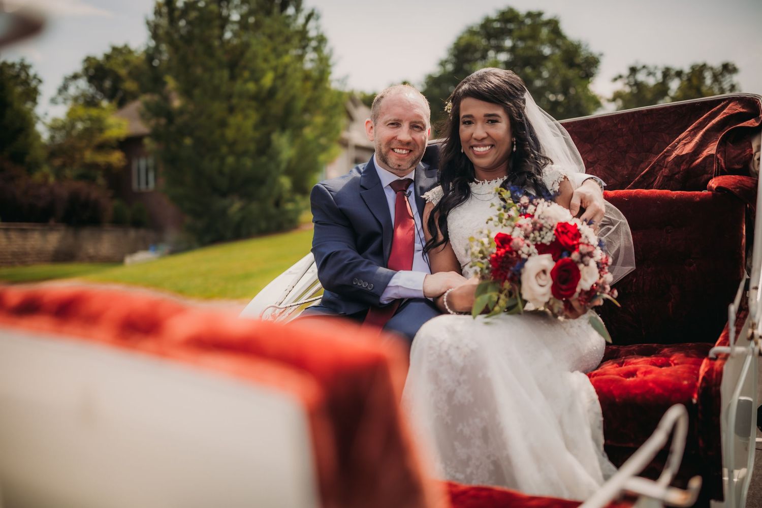 Newlyweds share a joyful moment in their elegant white carriage with red velvet interior.