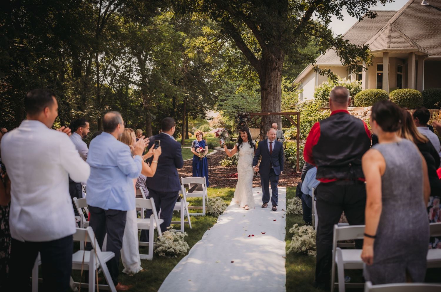 Wedding guests gather outdoors during a sunset ceremony with white chairs and natural surroundings.