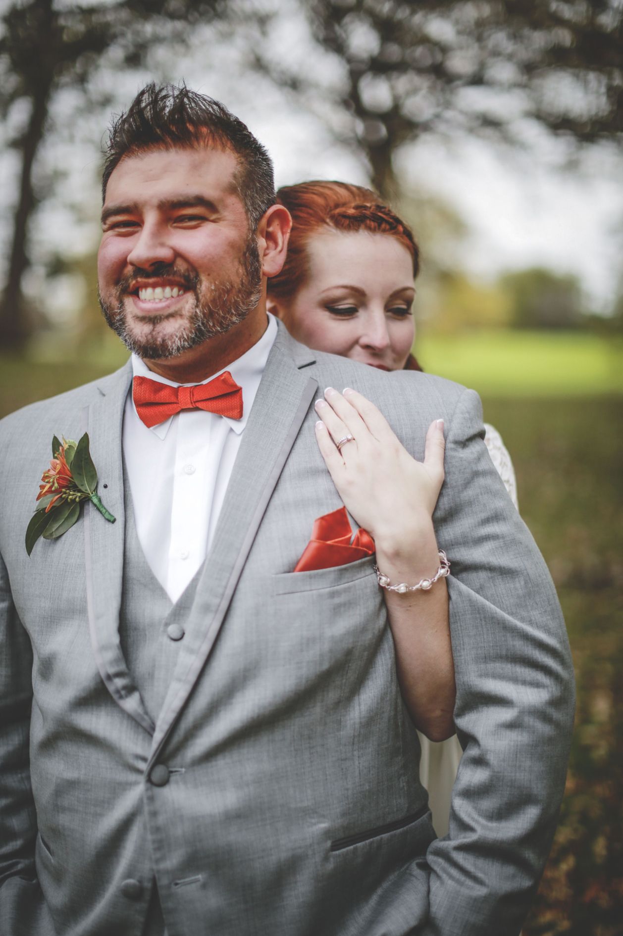 Candid wedding portrait of couple laughing together in grey attire with orange bowtie.