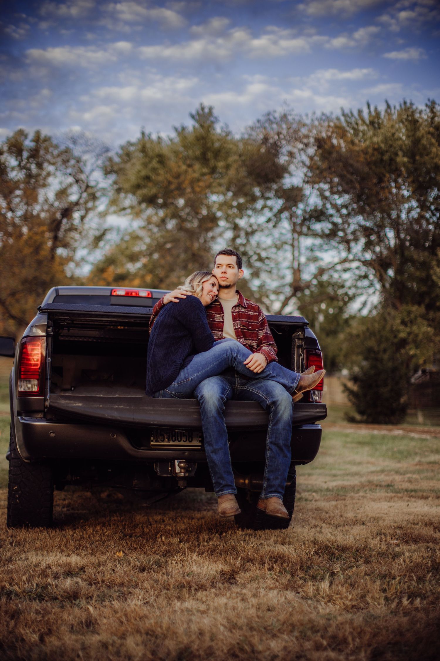 An intimate moment captured between a couple sitting on the back of their pickup truck in a rural setting.
