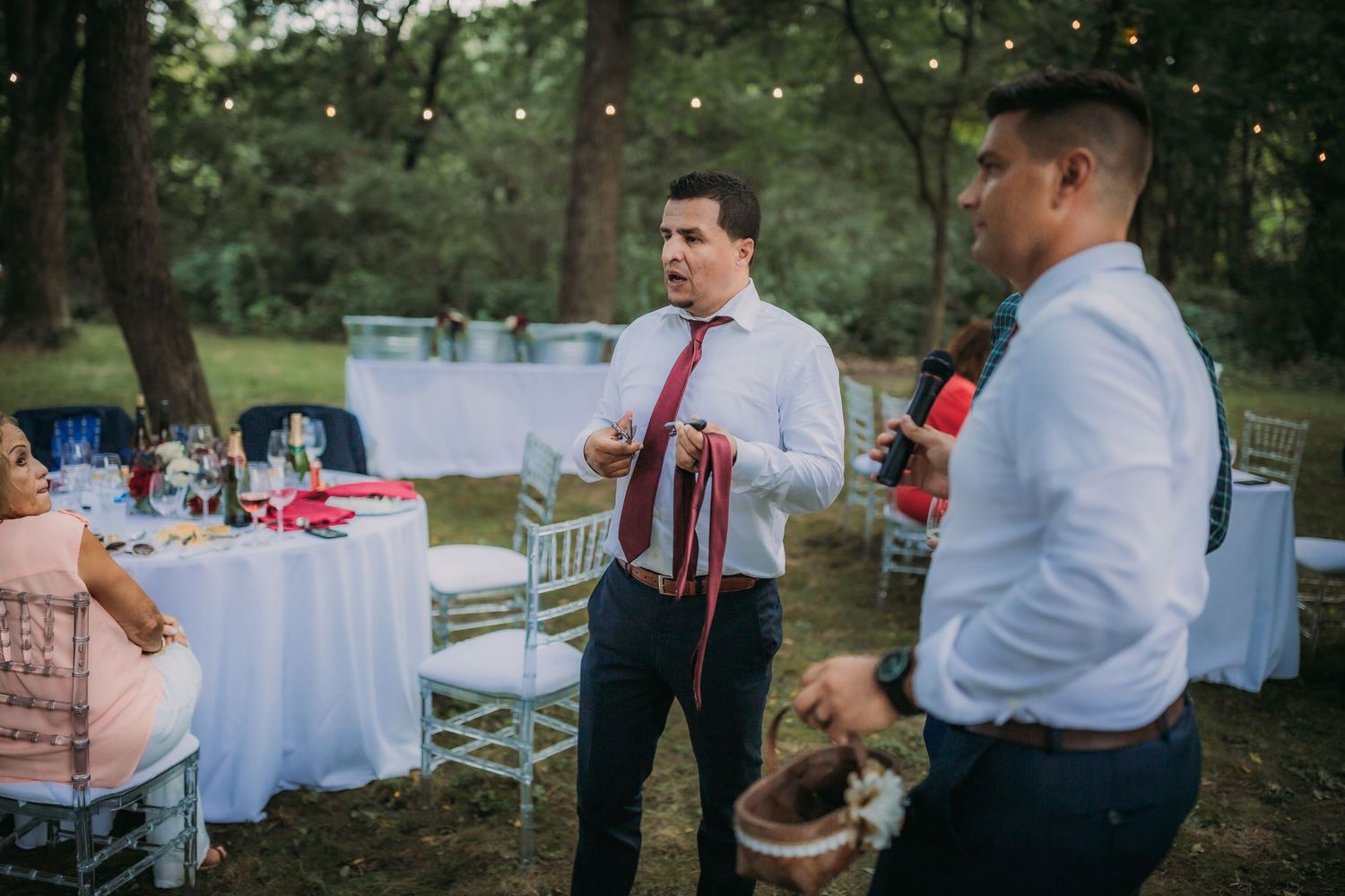 Guests in formal attire chatting at outdoor wedding reception with white tables in background.